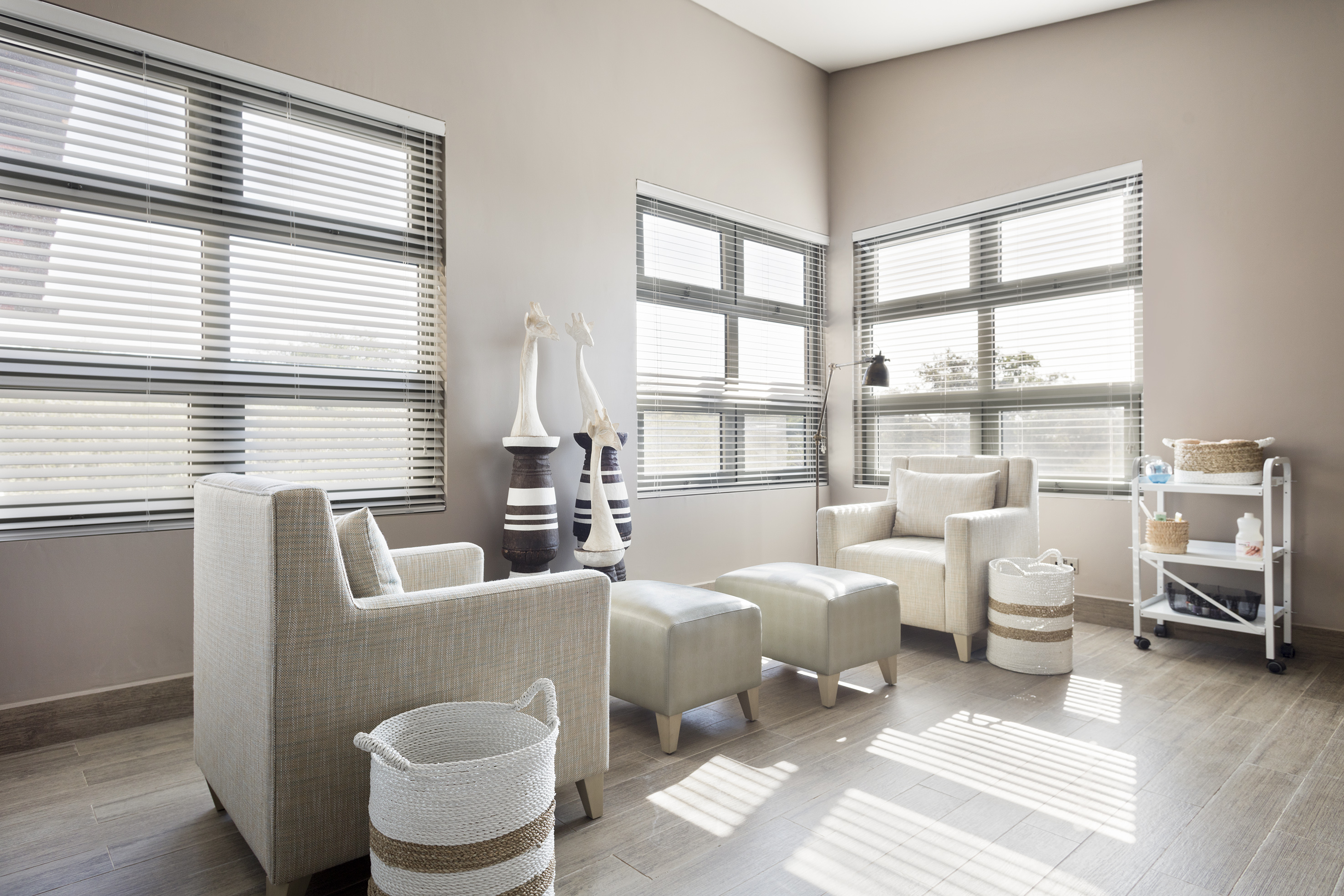 Modern living room with beige armchairs, horizontal blinds, and natural light.