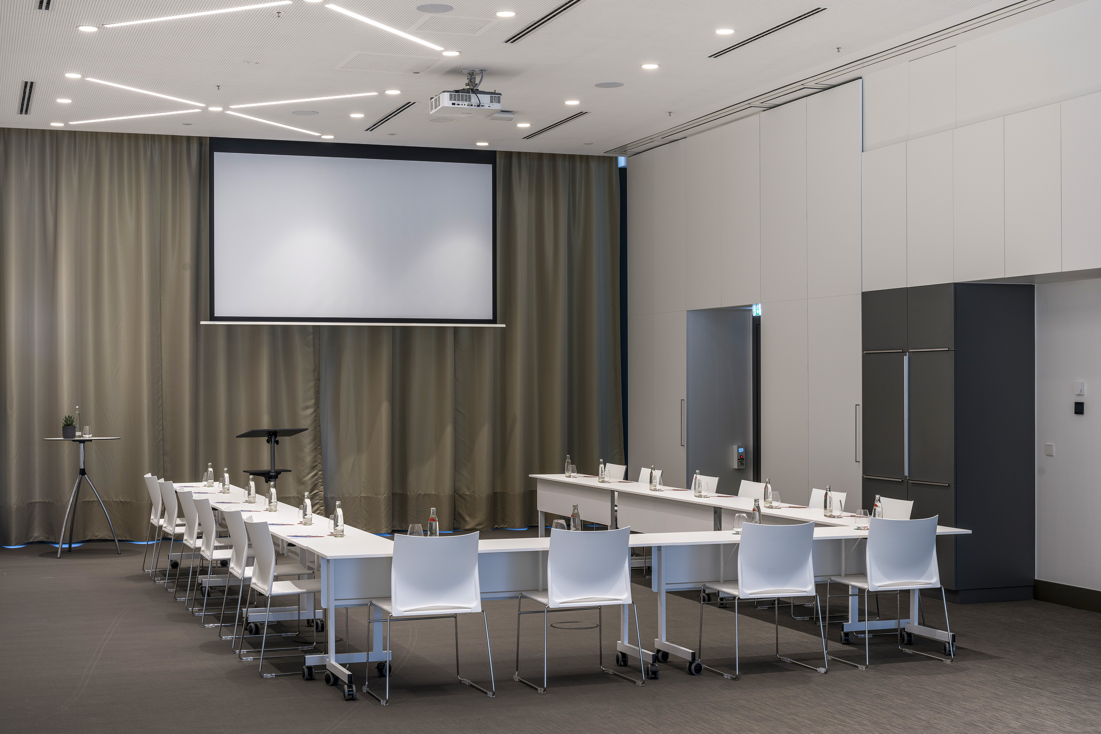 Modern U-shaped conference room, projection screen, and white chairs.