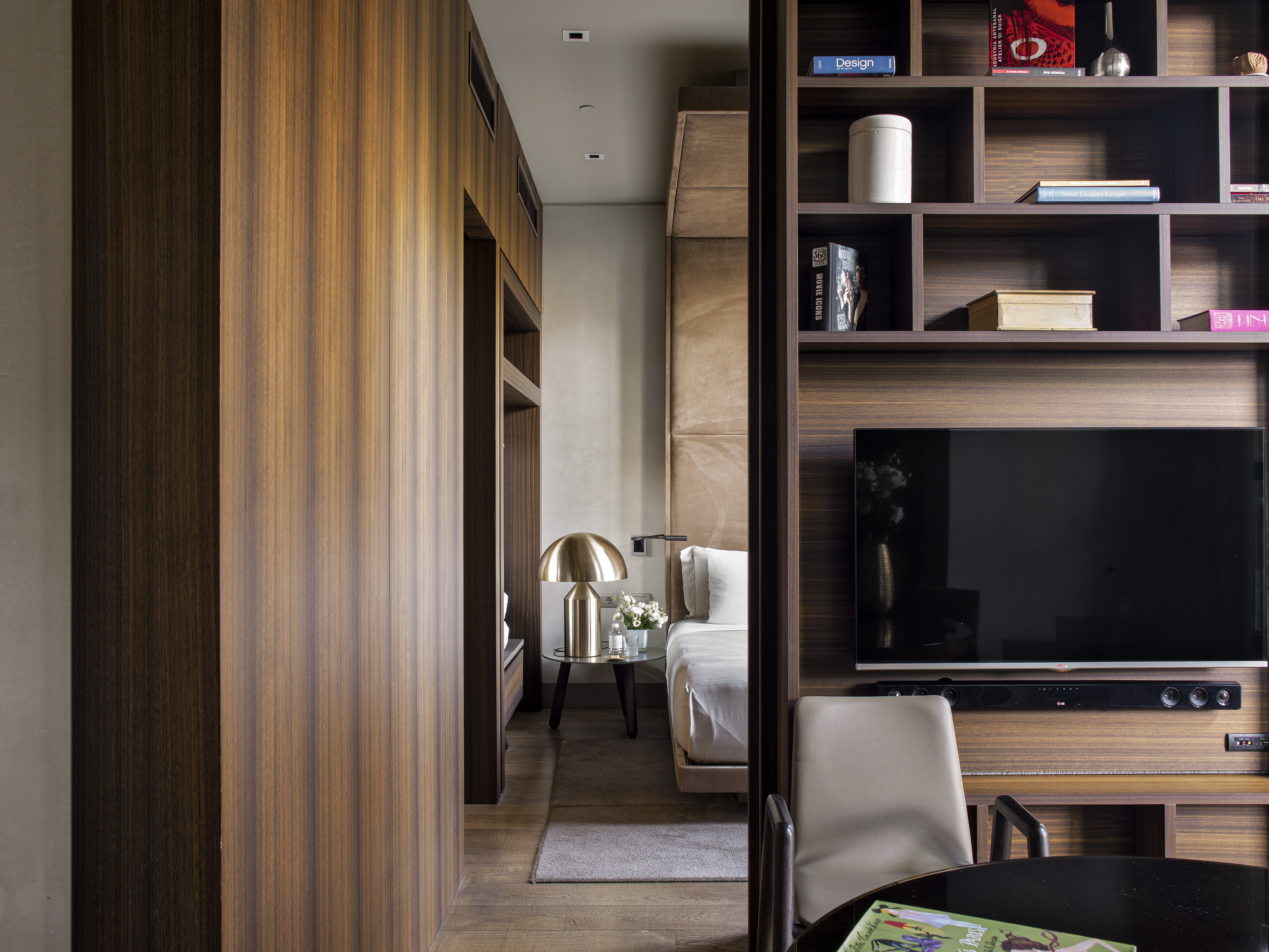Modern luxury bedroom interior with wood paneling, built-in TV, and elegant gold lamp.