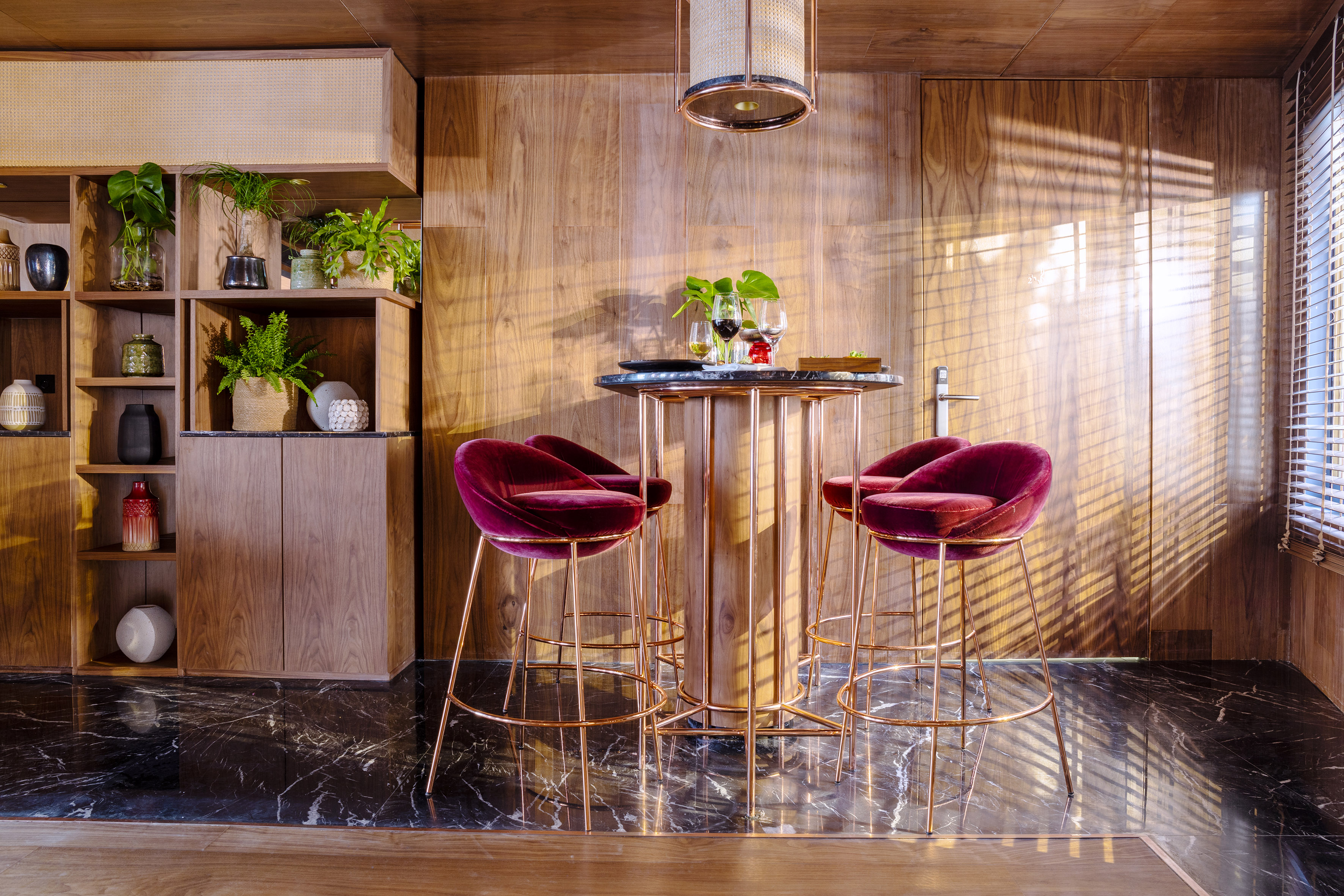 Luxury bar area with burgundy velvet stools, marble table, and wood panels.