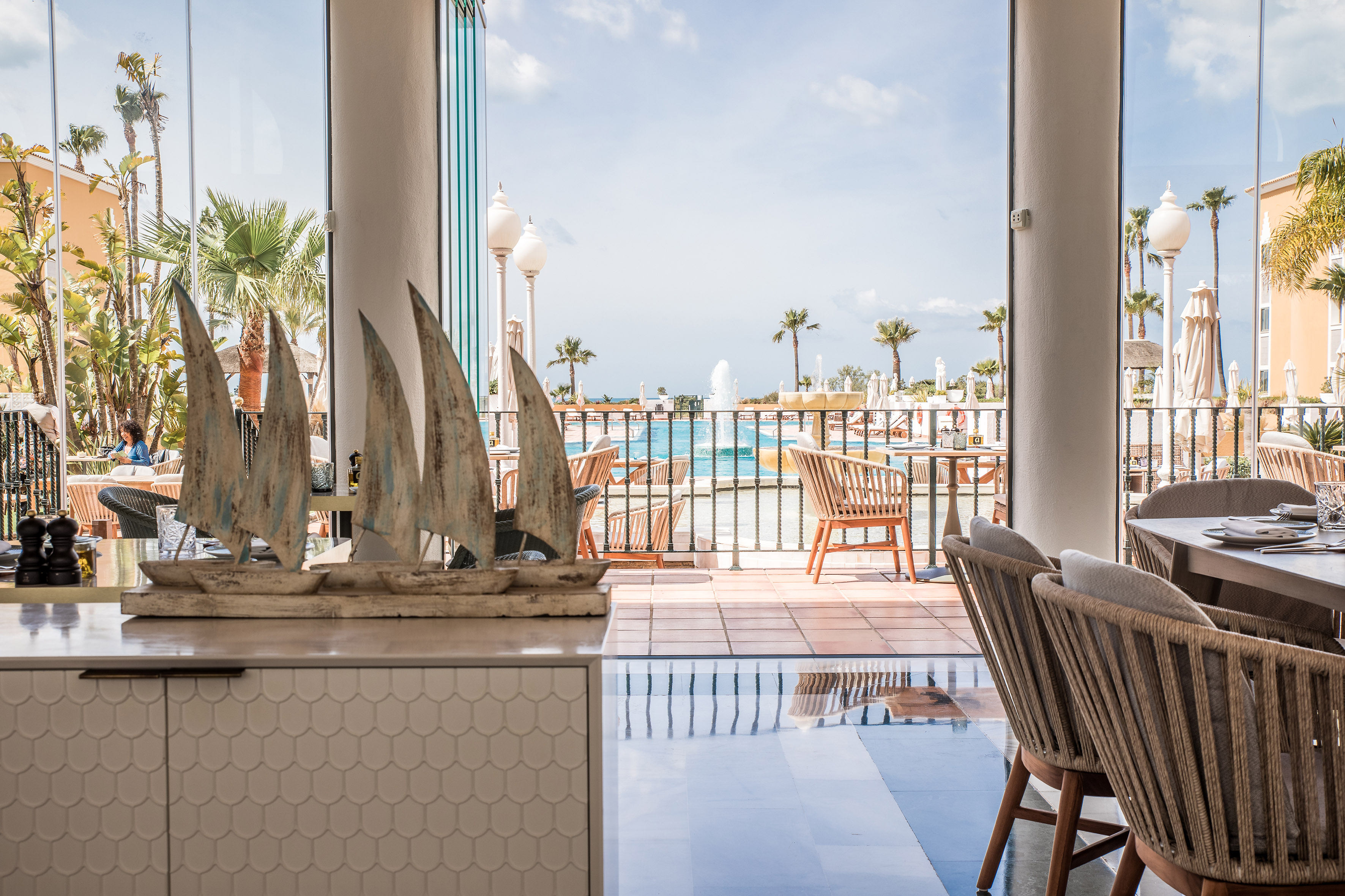 Restaurant with pool view, palm trees, and outdoor resort dining area.