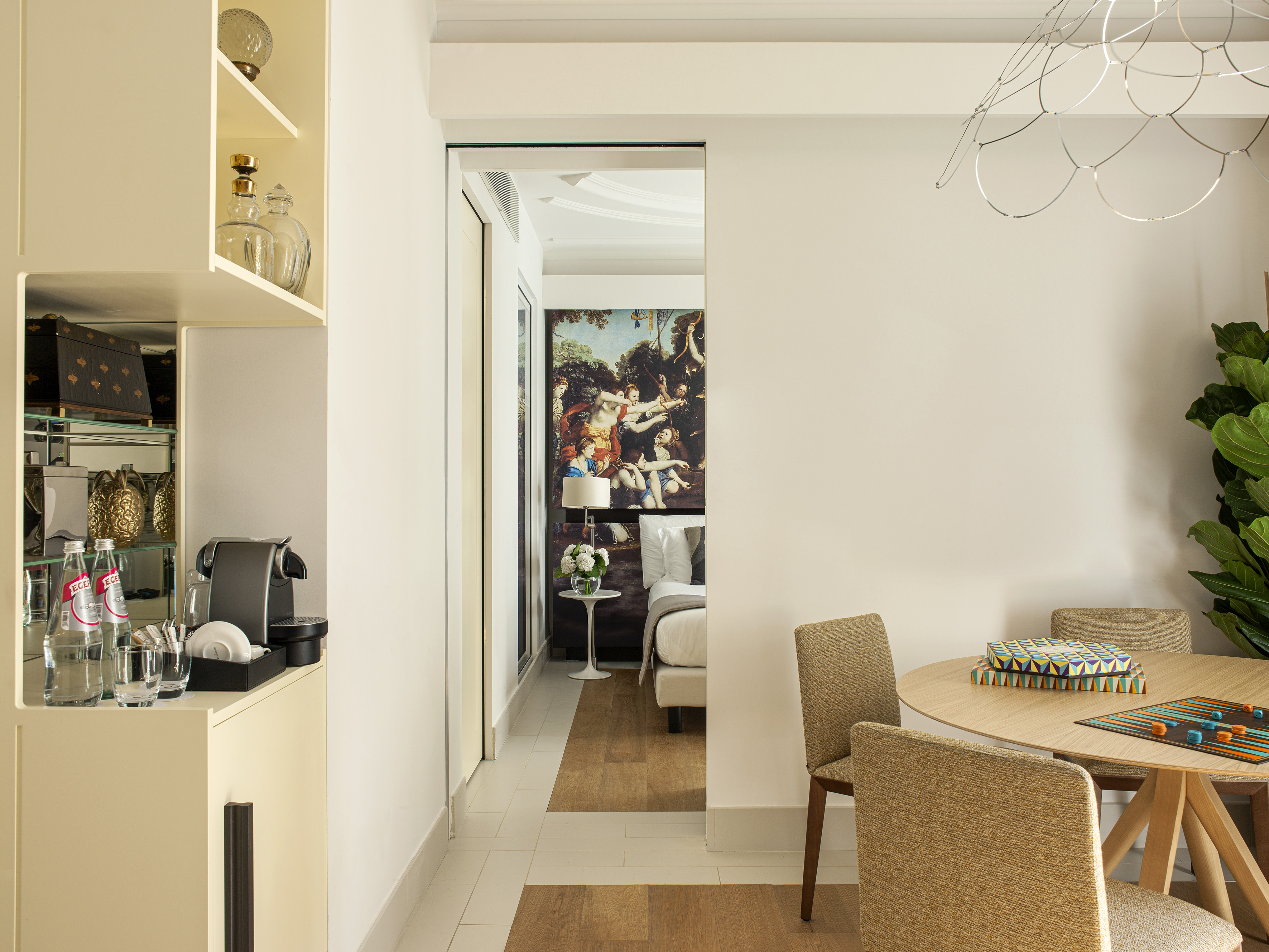 Modern hotel suite with dining table, minibar, and bedroom view.