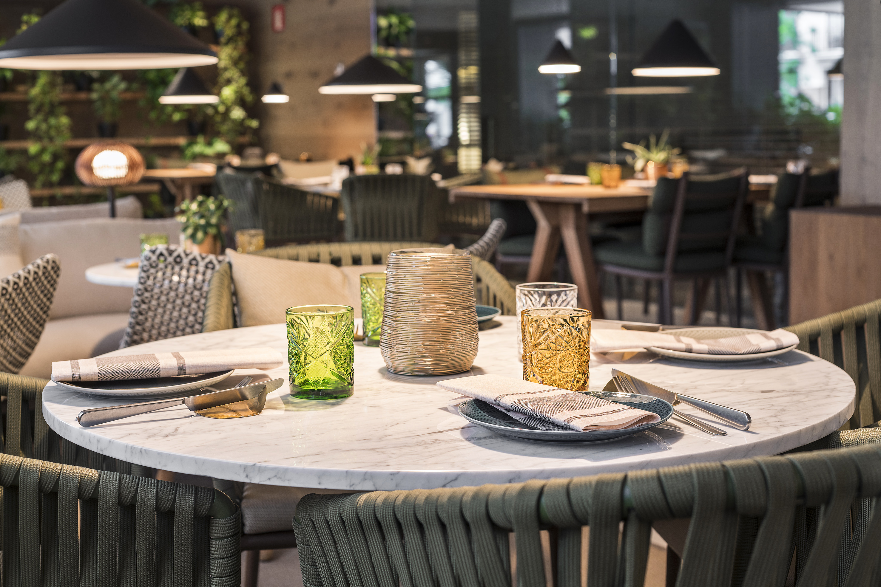 Modern restaurant interior: set dining table, green woven chairs, marble top.