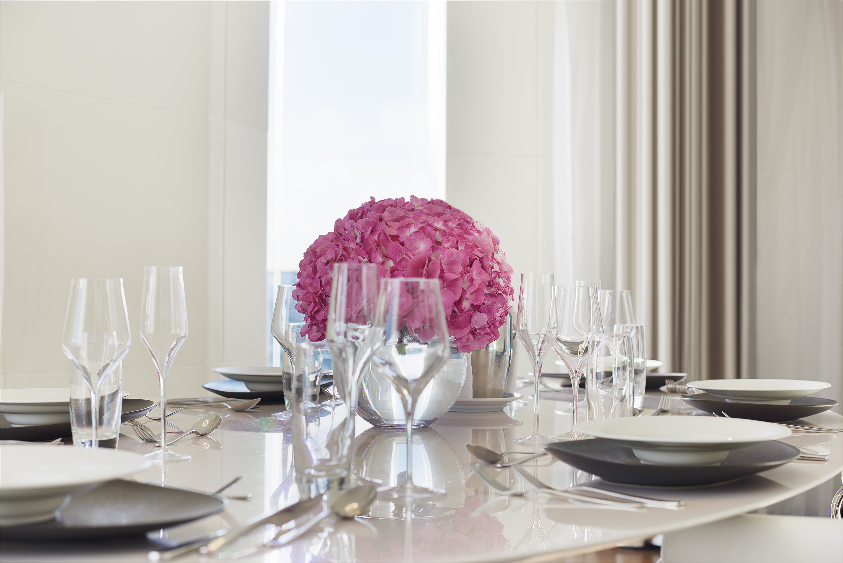 Elegant dining table with modern place settings and vibrant pink hydrangea centerpiece.