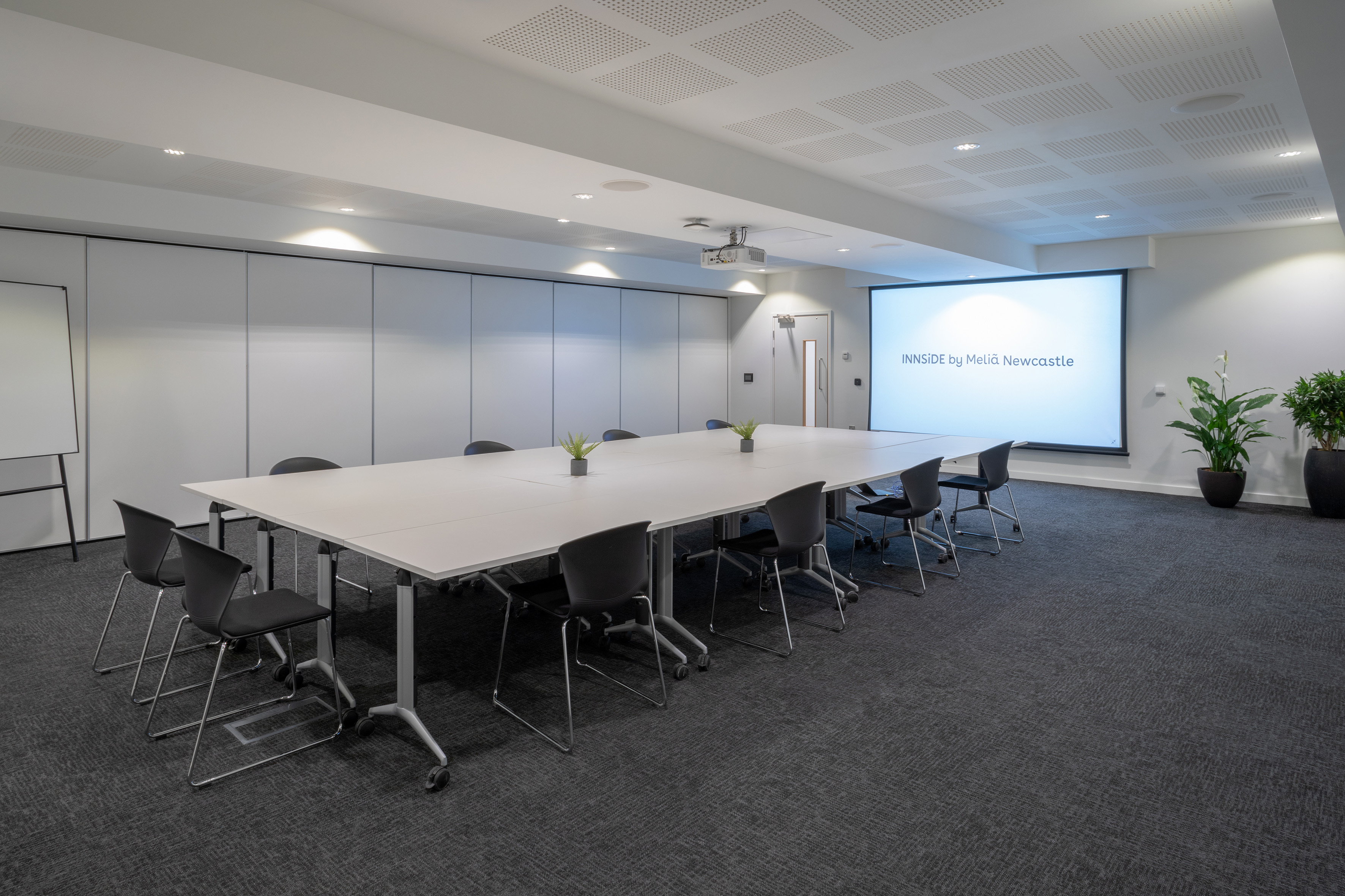 Modern meeting room with long table, black chairs, and projector screen.