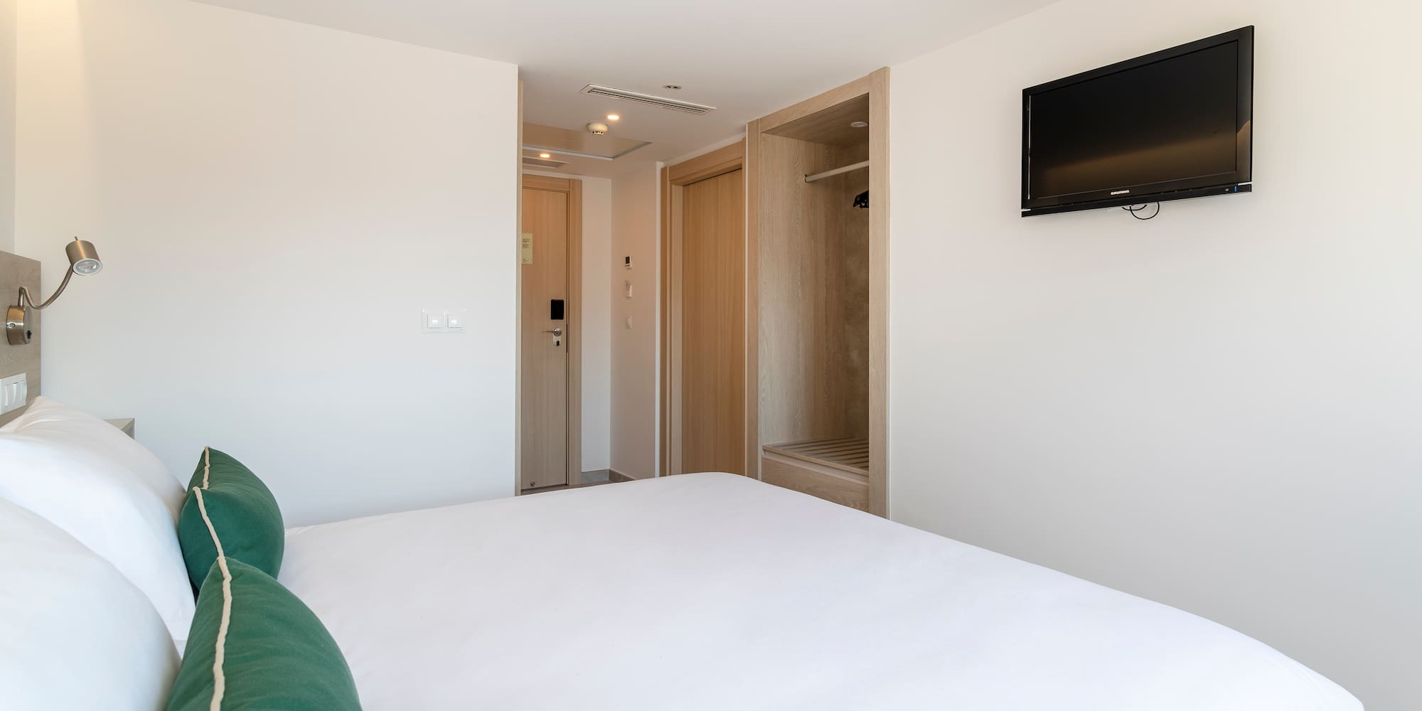 a bed with a green pillow and a tv on the wall