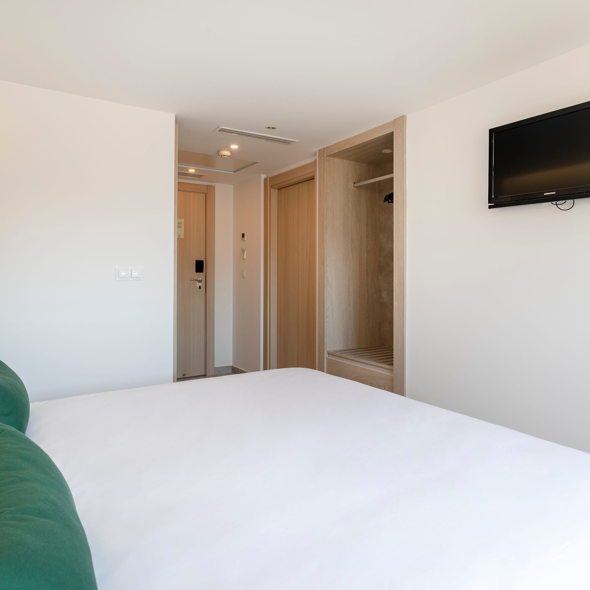 a bed with a green pillow and a tv on the wall