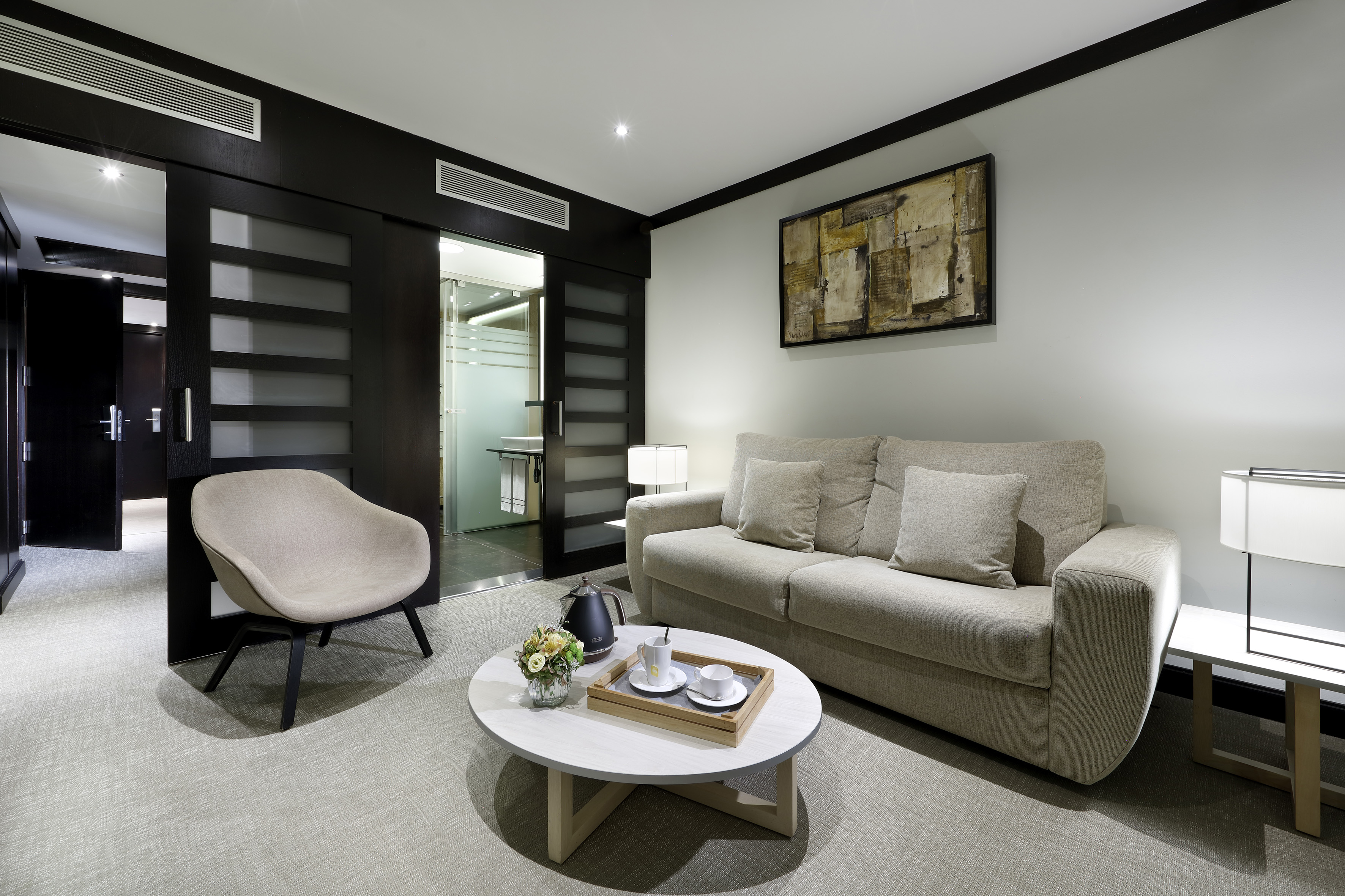 Modern hotel suite living room with light sofa, armchair, and coffee table.