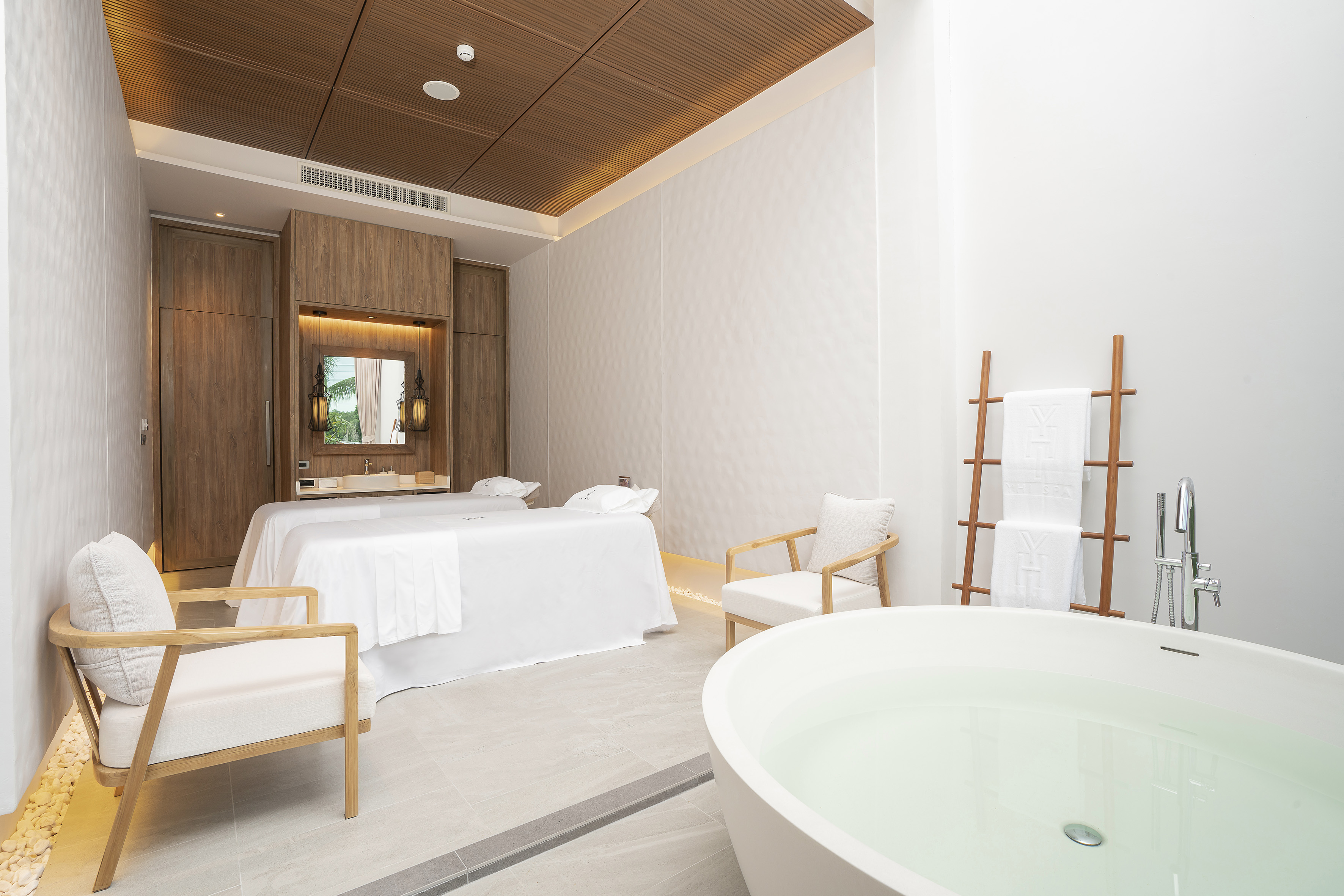 Spa treatment room with two massage beds, freestanding tub, and wood ceiling.