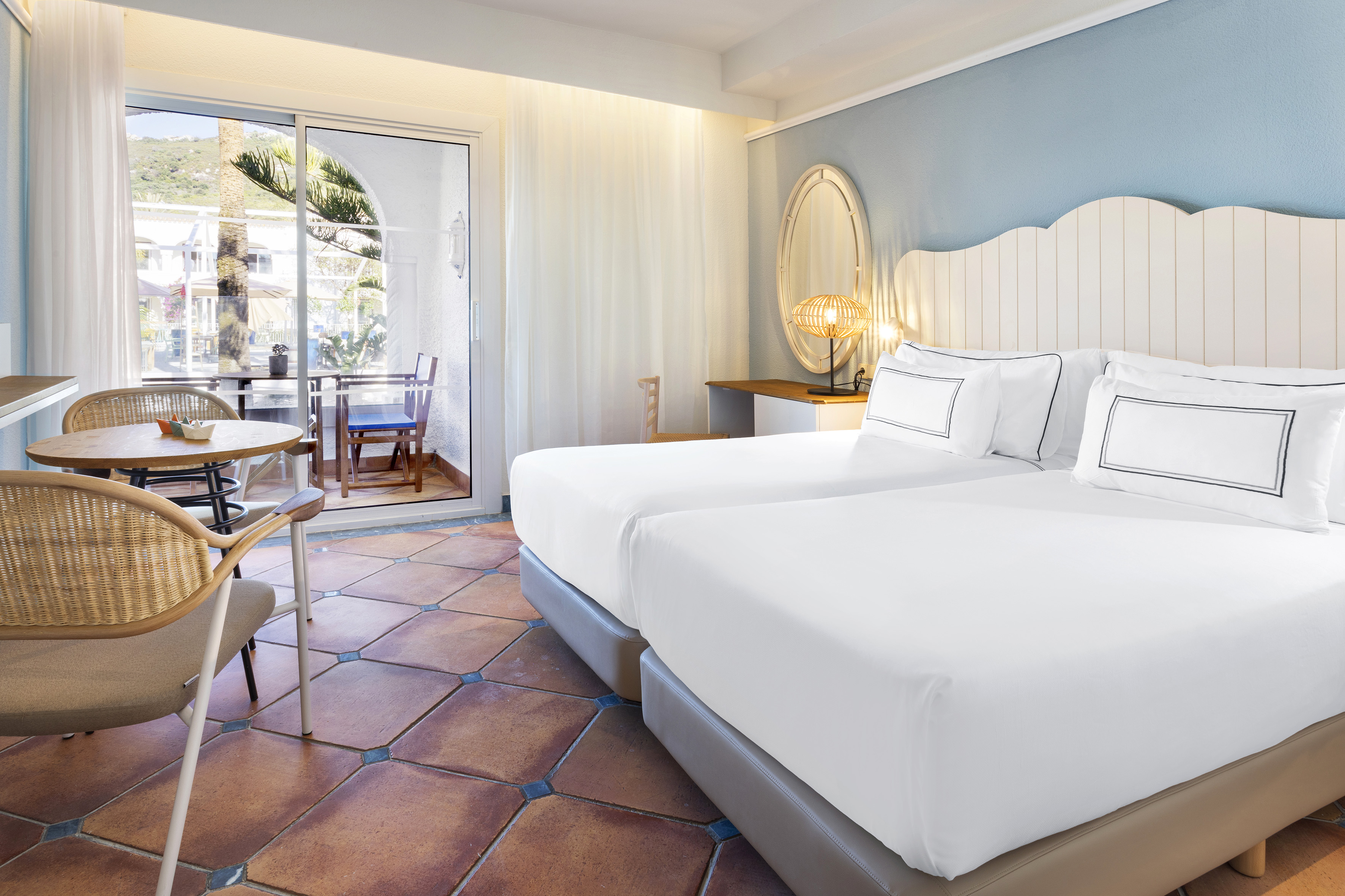 Mediterranean hotel room with twin beds, terracotta floor, and balcony.