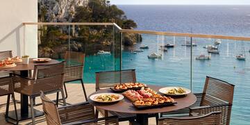 a table with food on it and chairs on a balcony overlooking water
