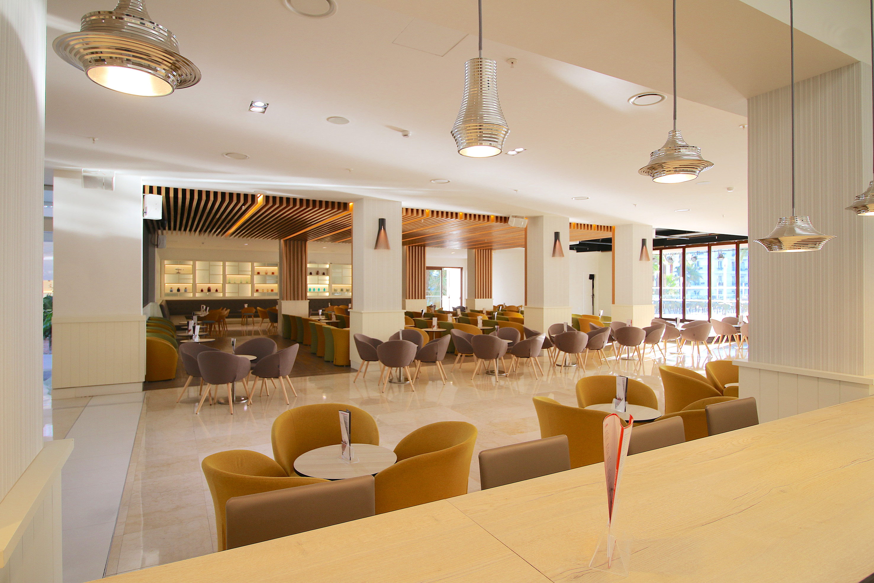 Bright modern hotel lounge with yellow and grey seating, wood accents.
