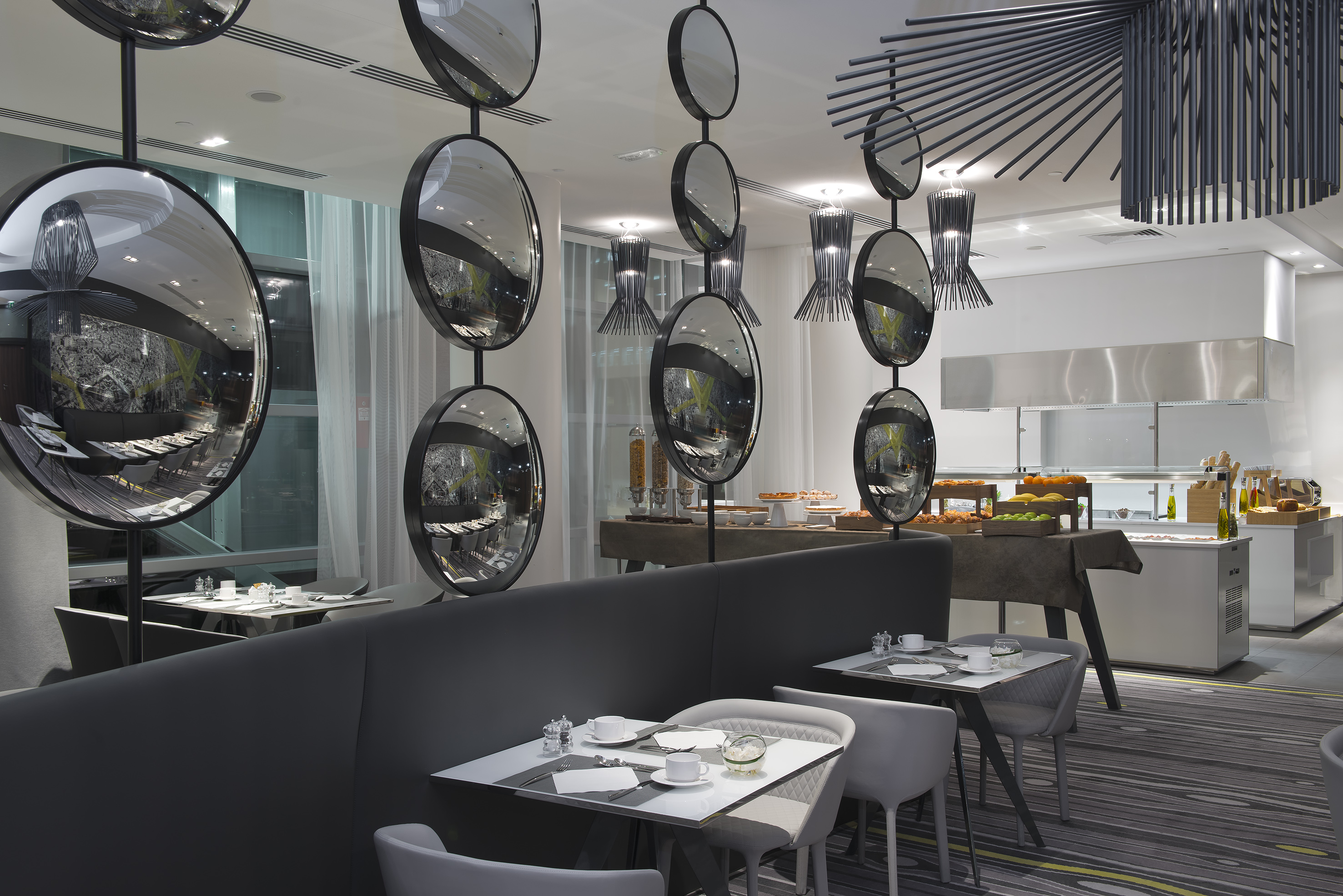 Modern hotel dining, hanging circular mirrors, buffet, and set tables.