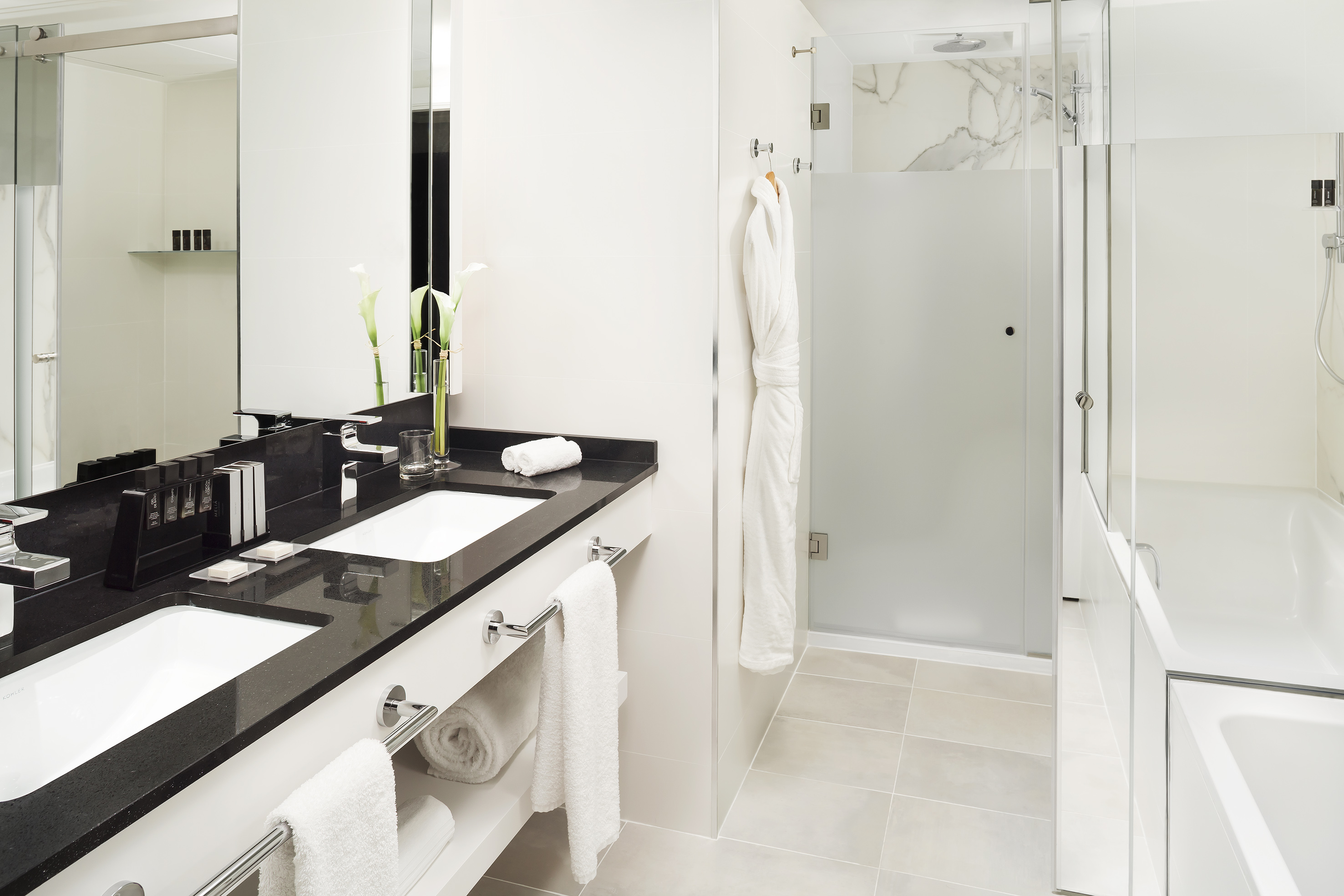 Sleek hotel bathroom with double sink, black counter, glass shower, bathtub.