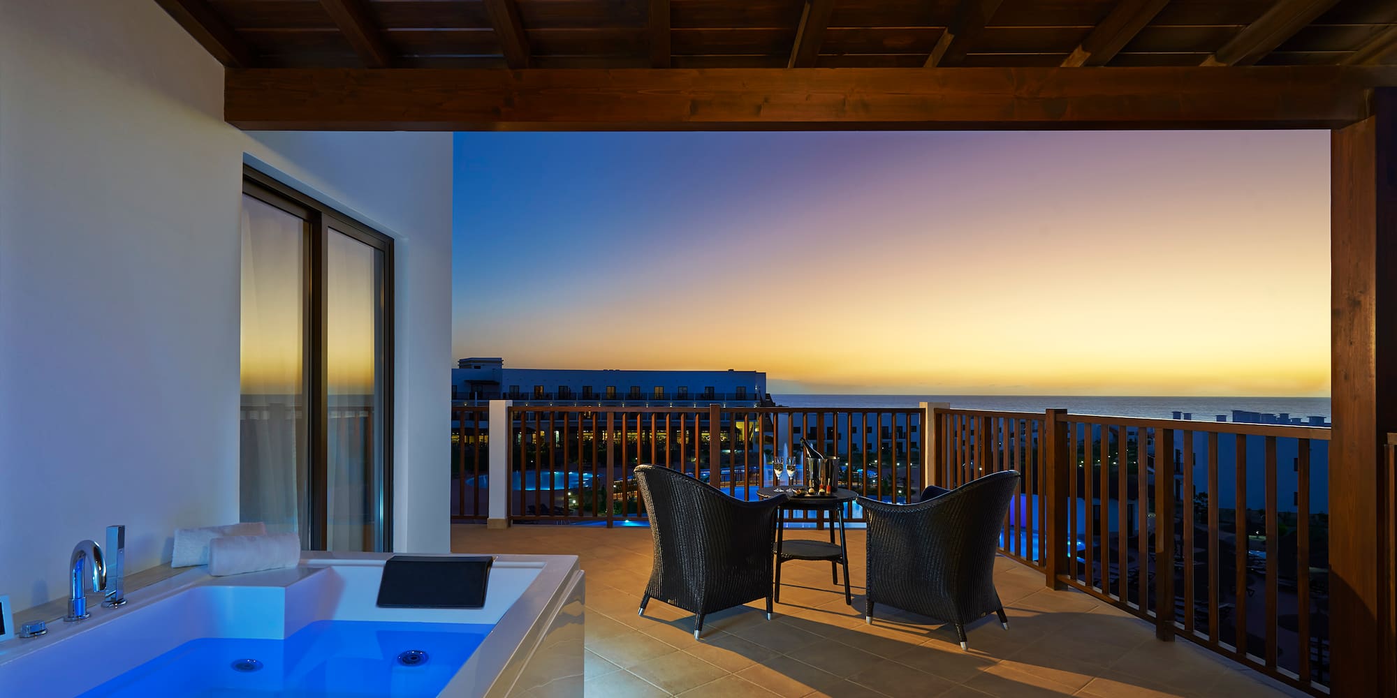 a deck with a hot tub and chairs overlooking the ocean