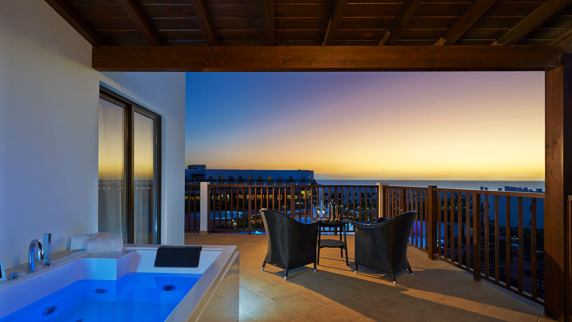 a deck with a hot tub and chairs overlooking the ocean