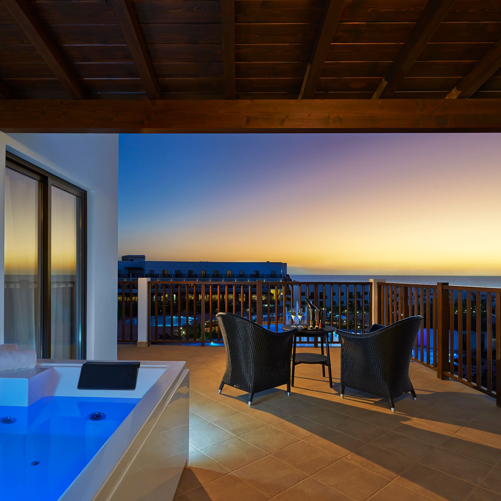 a deck with a hot tub and chairs overlooking the ocean