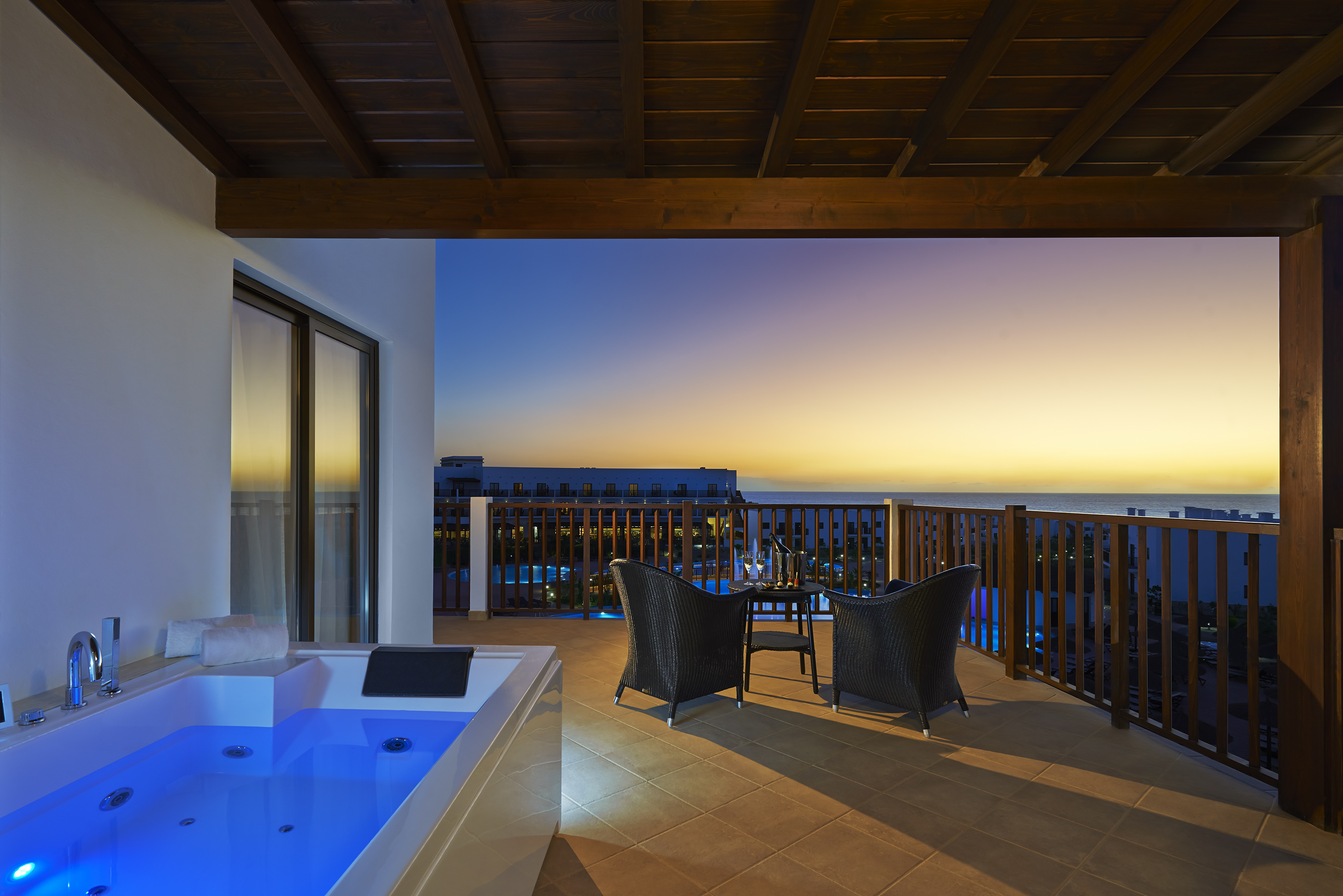 a deck with a hot tub and chairs overlooking the ocean