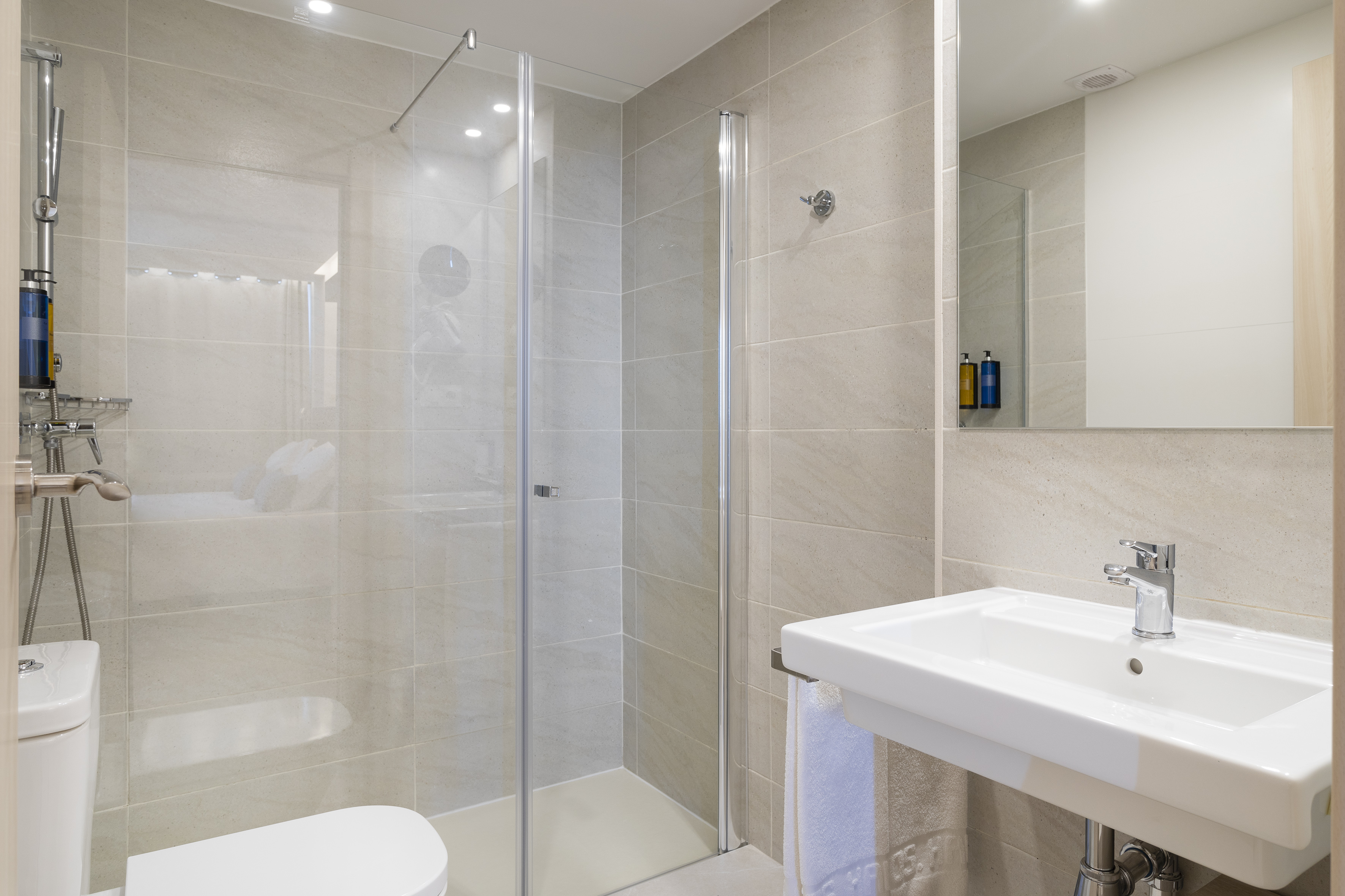Modern bathroom with glass shower, white toilet, sink, light grey tiles.