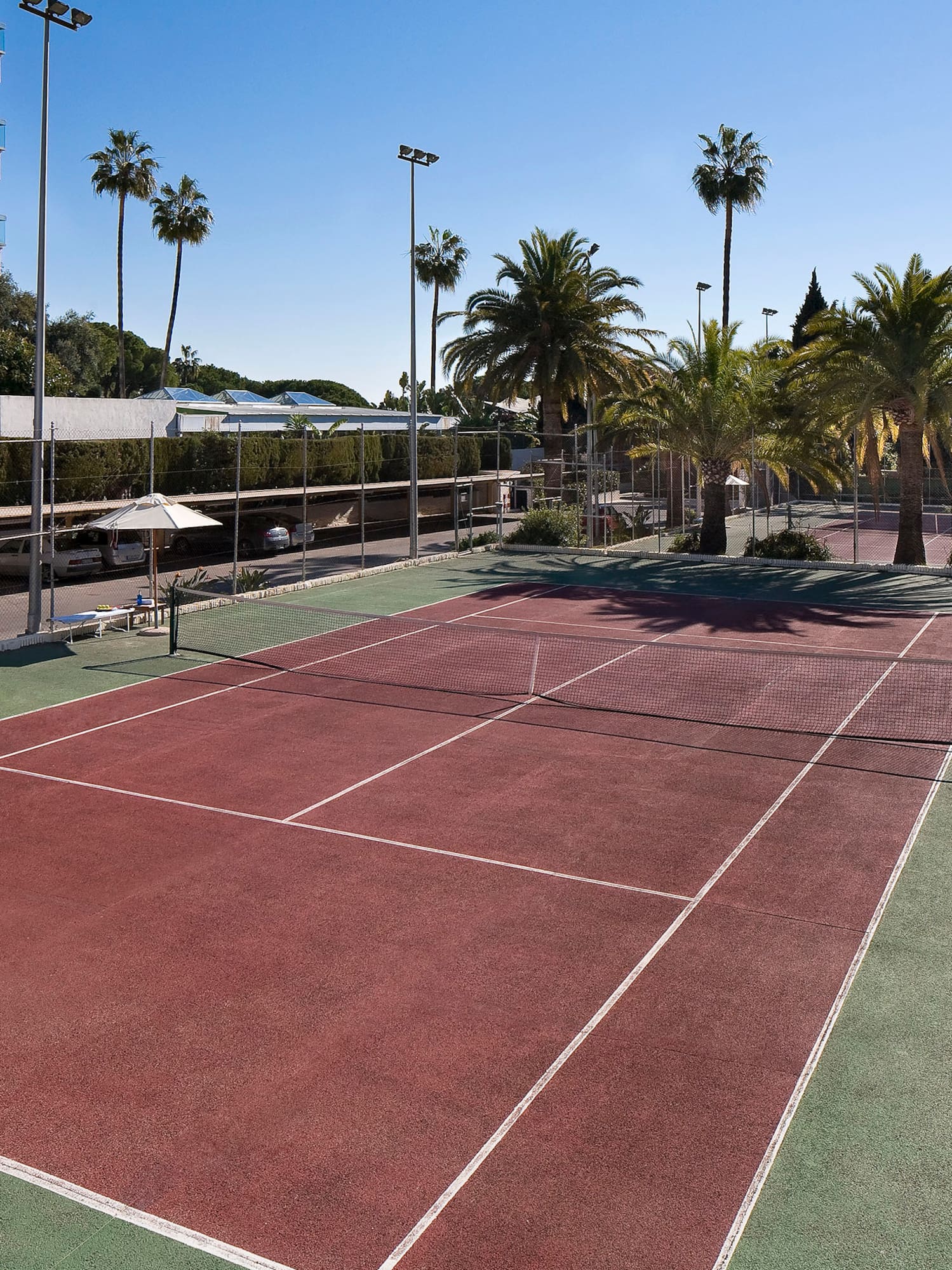 a tennis court with palm trees and buildings