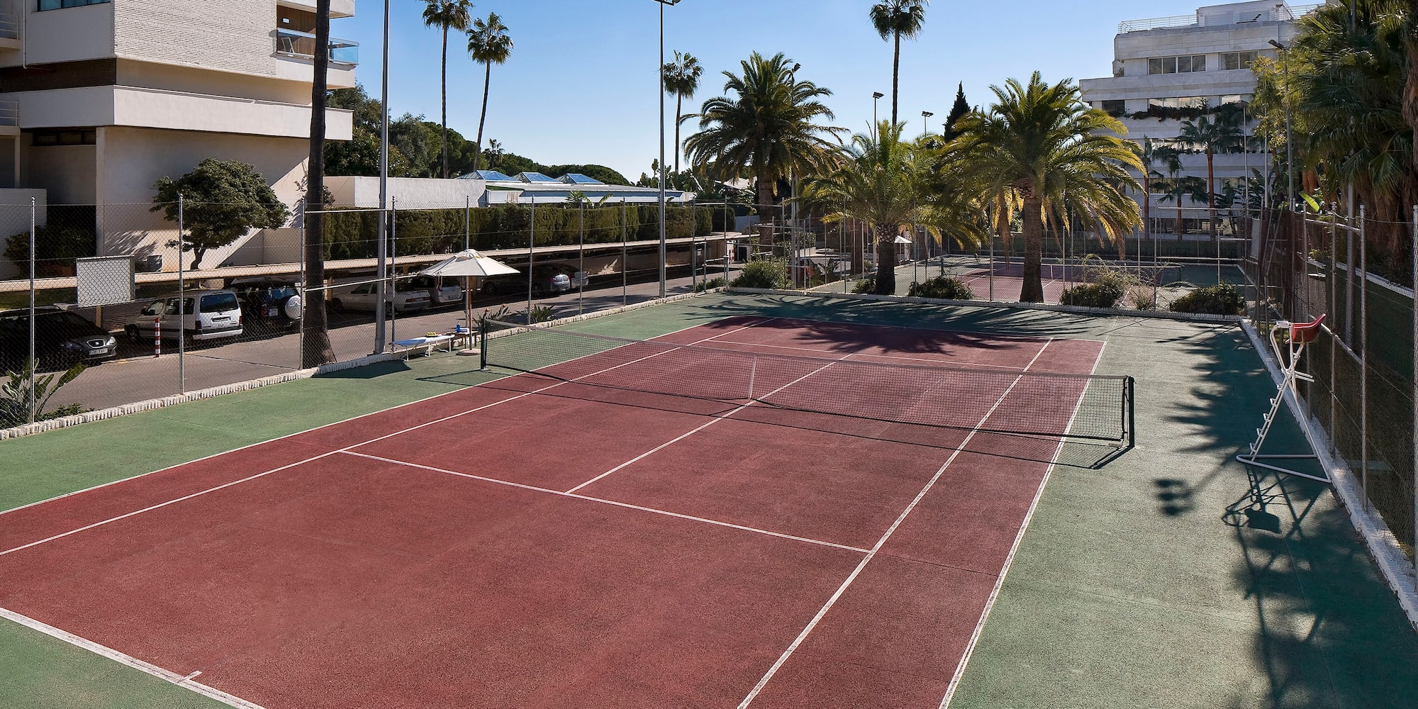 a tennis court with palm trees and buildings