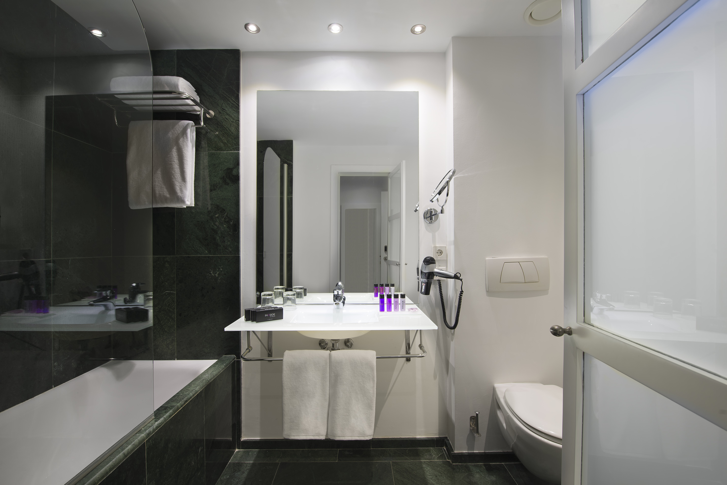 Contemporary hotel bathroom with green marble, bathtub, modern vanity, and white toilet.