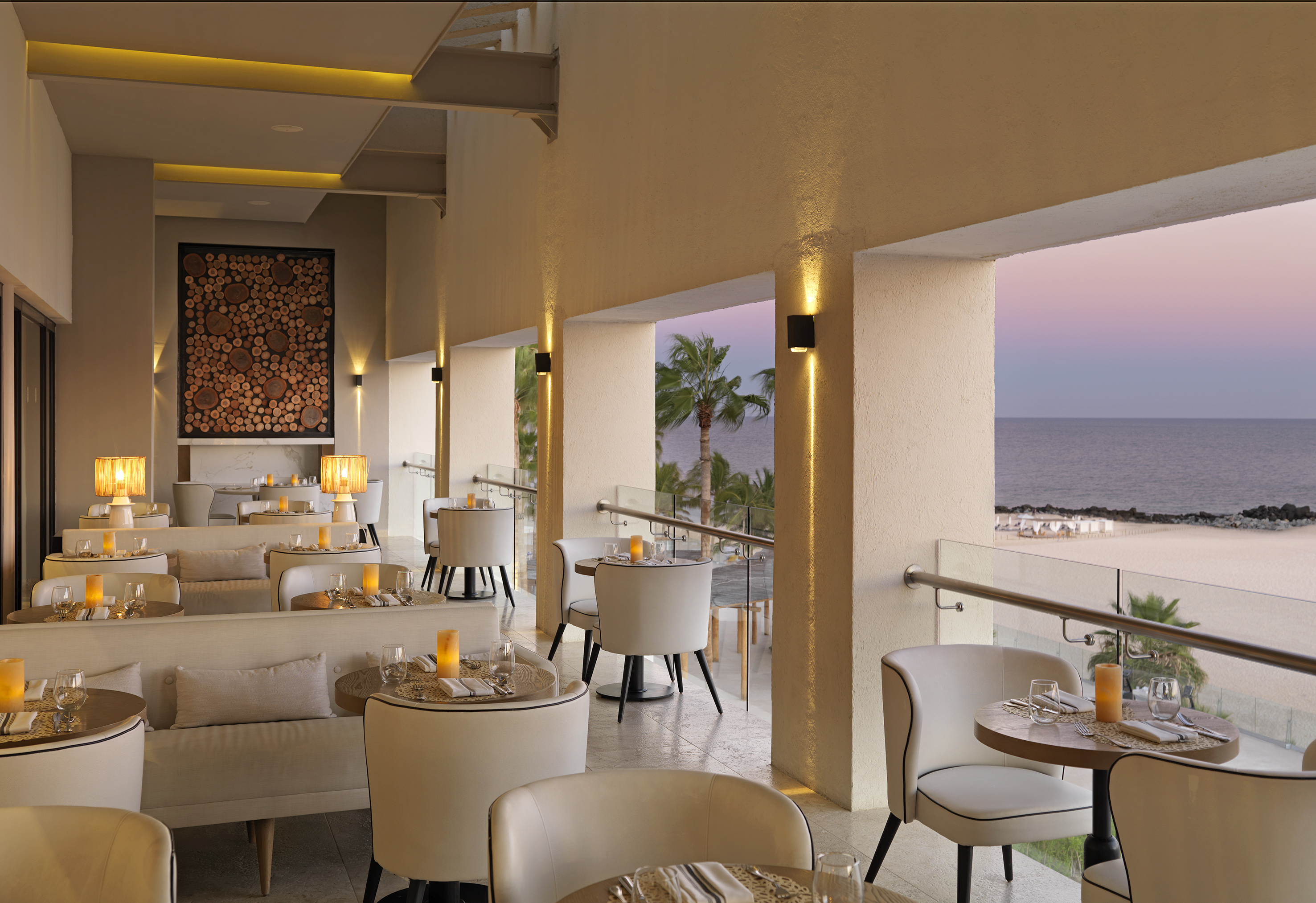 Luxury oceanfront restaurant terrace with modern dining, sunset beach view.
