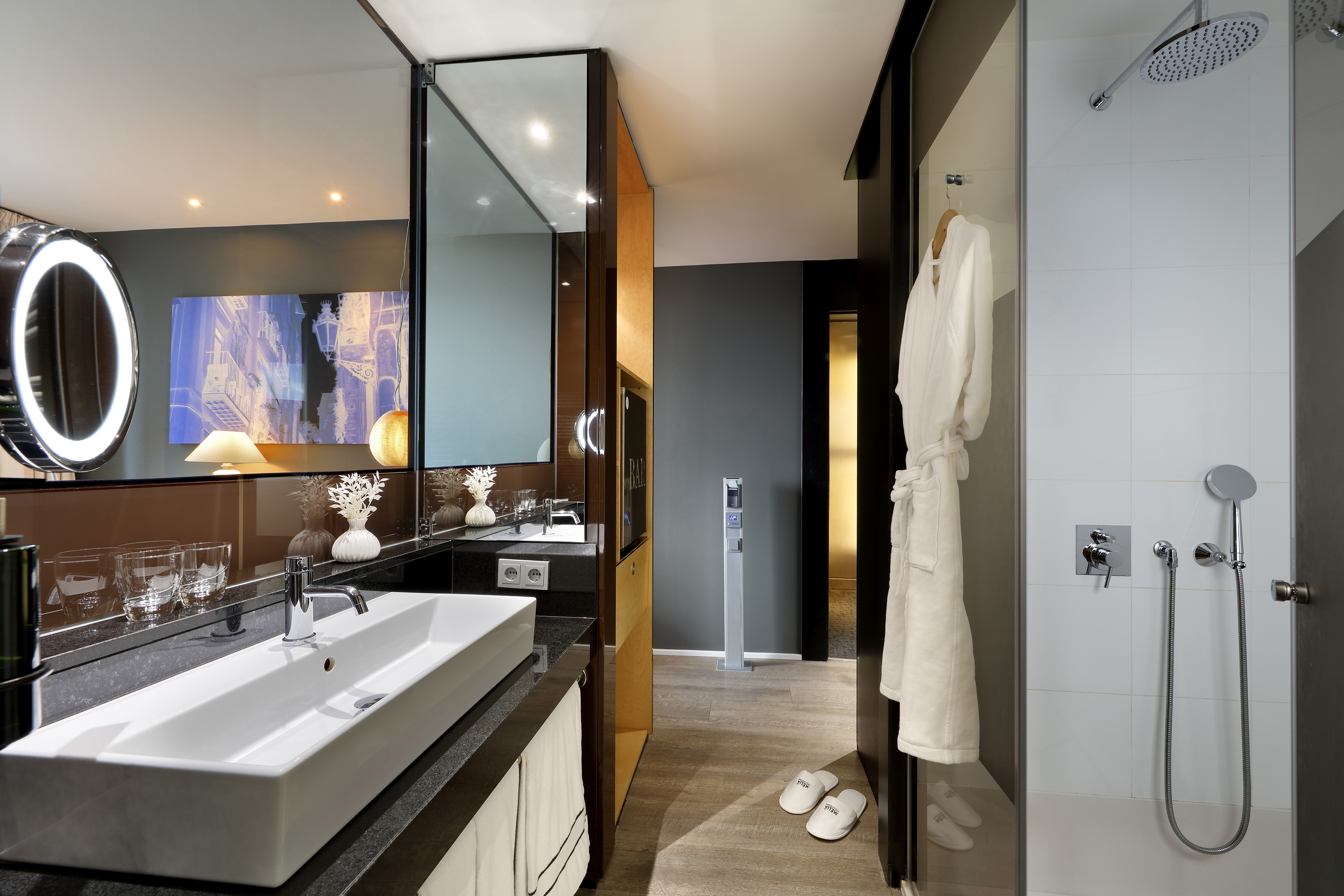Luxury hotel bathroom with illuminated vanity, walk-in shower, and bathrobe.