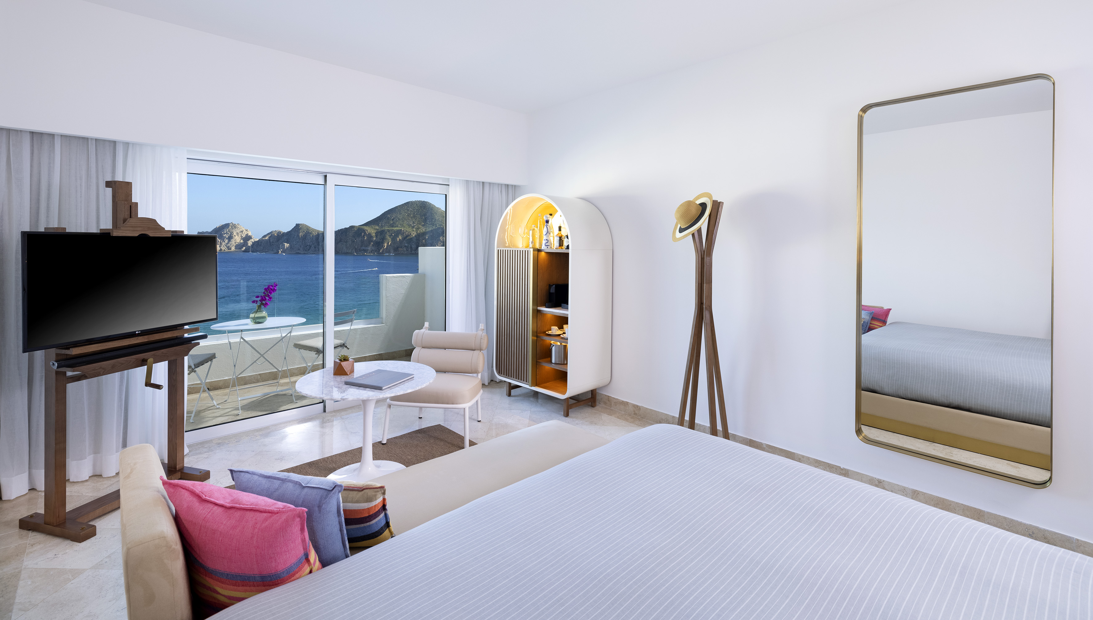 Modern ocean view suite with balcony, TV, minibar, and coastal landscape.