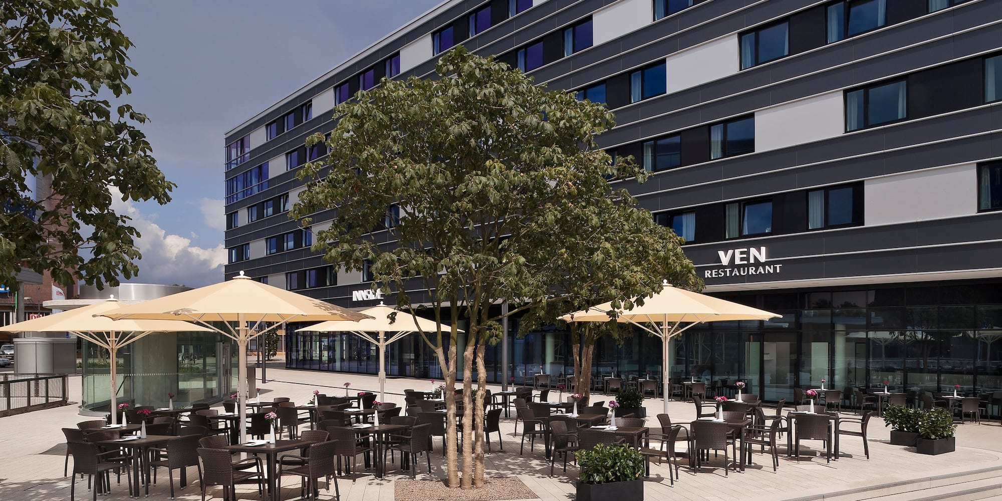 Terraza exterior del restaurante VEN con mesas, sombrillas y edificio moderno.