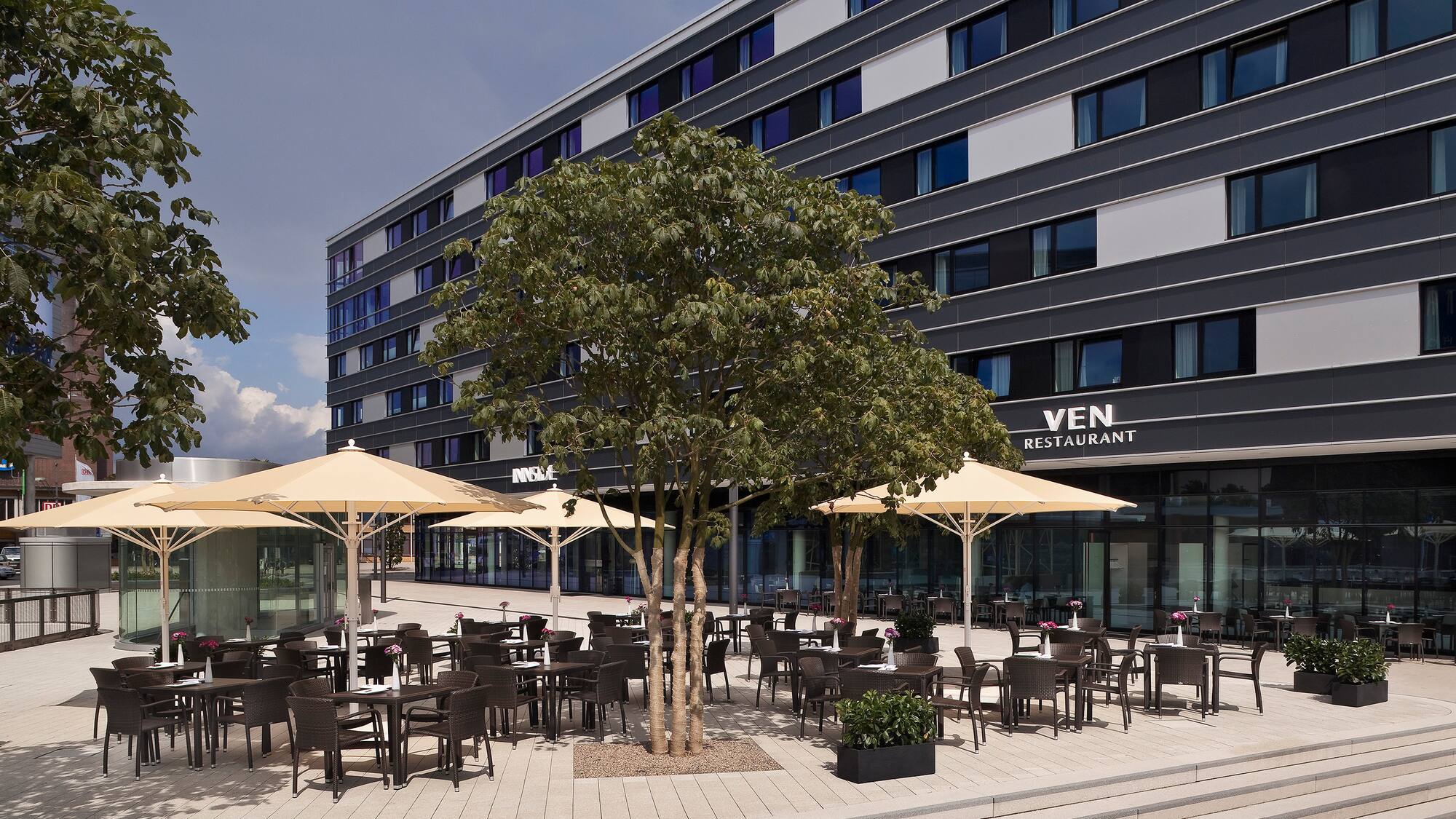 Terraza exterior del restaurante VEN con mesas, sombrillas y edificio moderno.