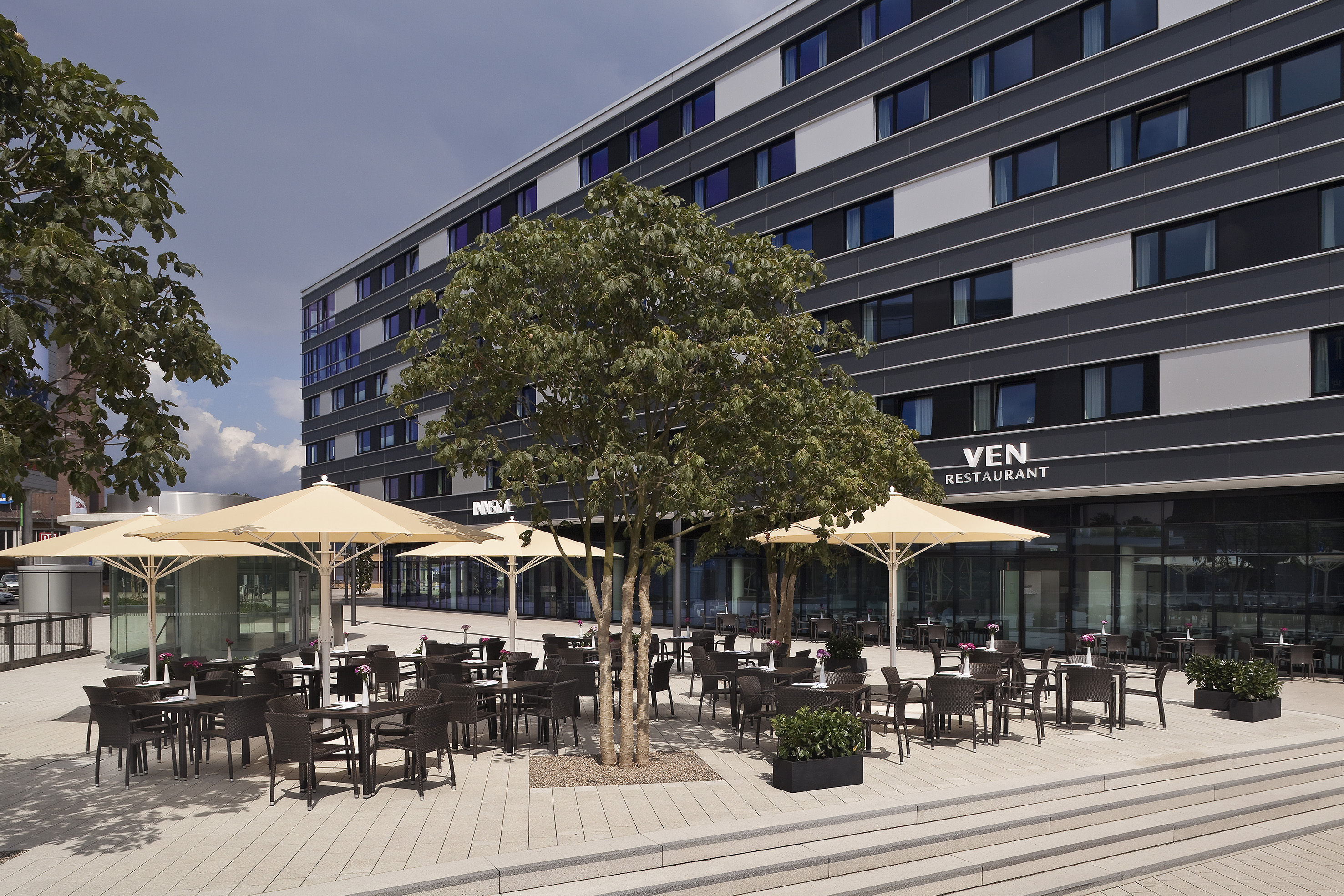 Terraza exterior del restaurante VEN con mesas, sombrillas y edificio moderno.