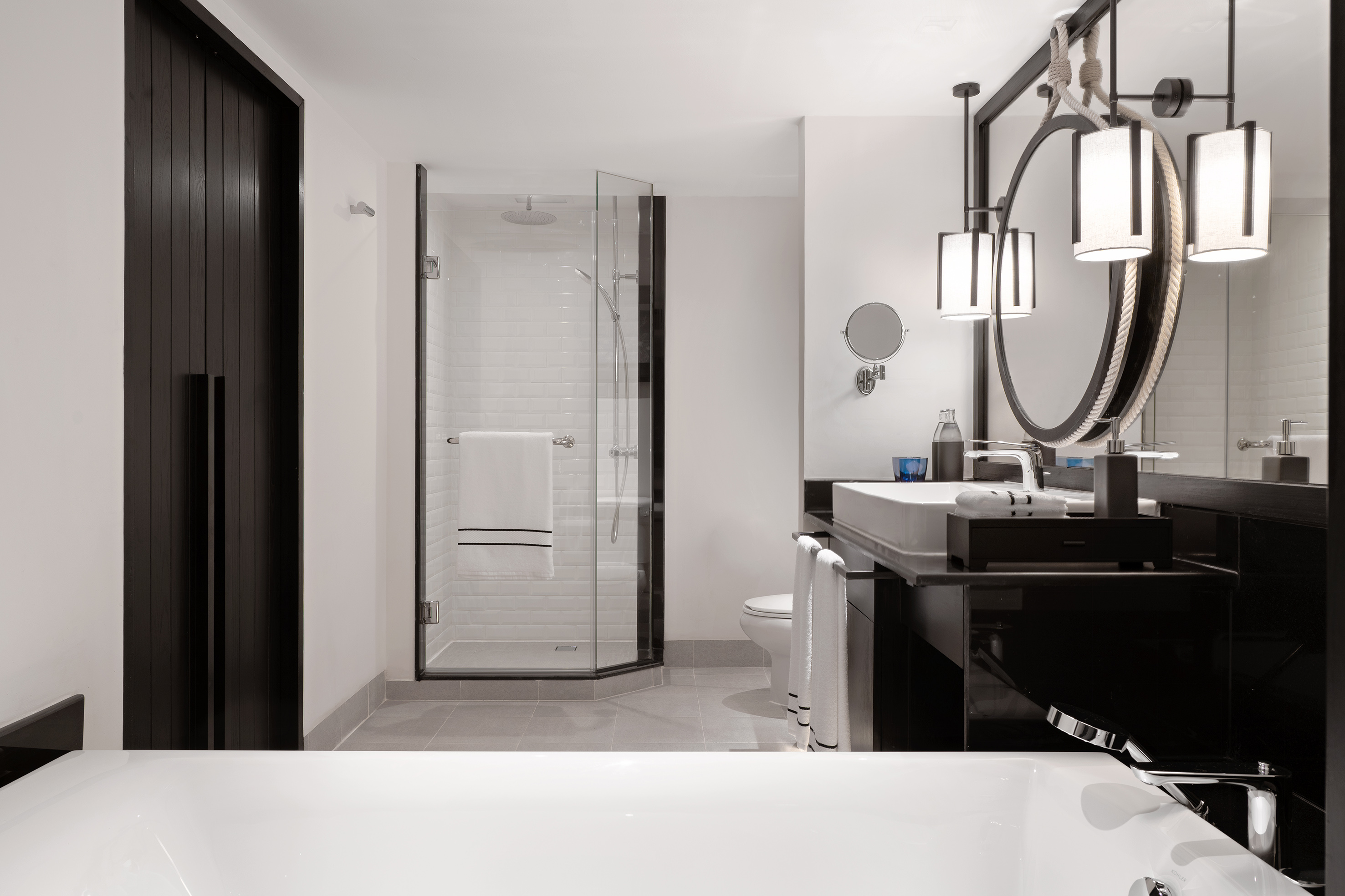 Modern bathroom with black vanity, white tub, glass shower, and round mirror.