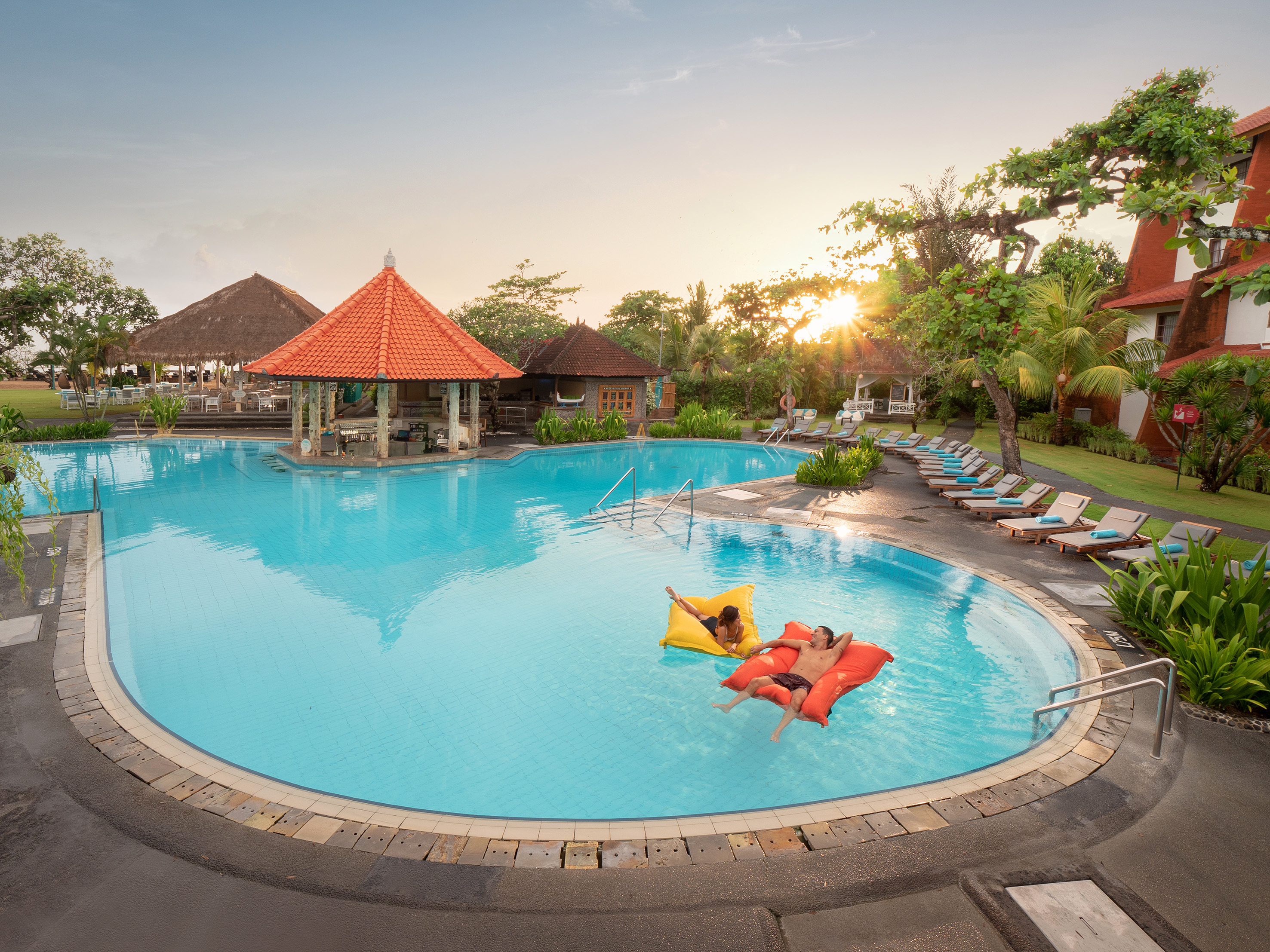 a pool with people floating on mattresses and lounge chairs