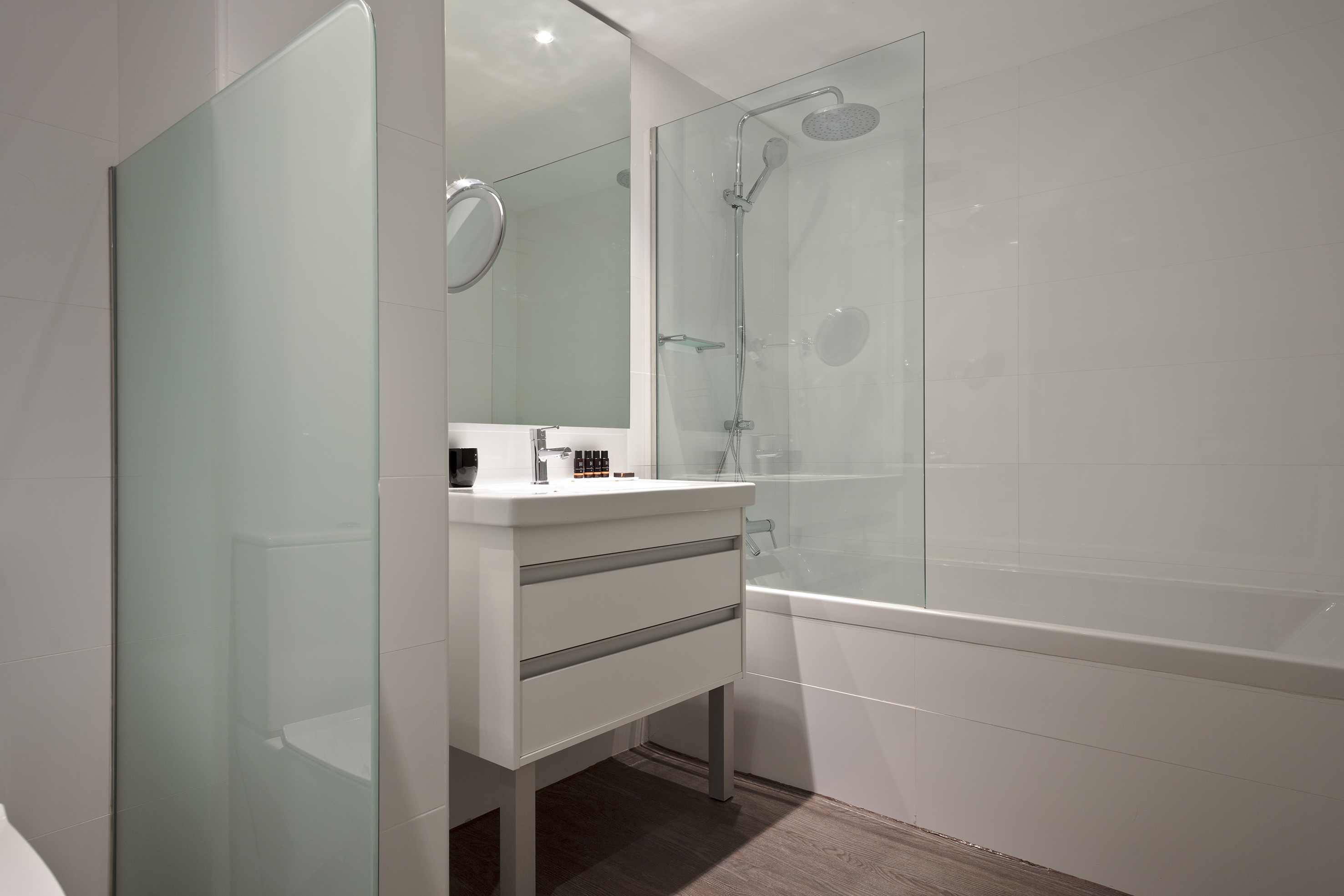 Modern white tiled bathroom with vanity, mirror, and shower-bathtub combo.