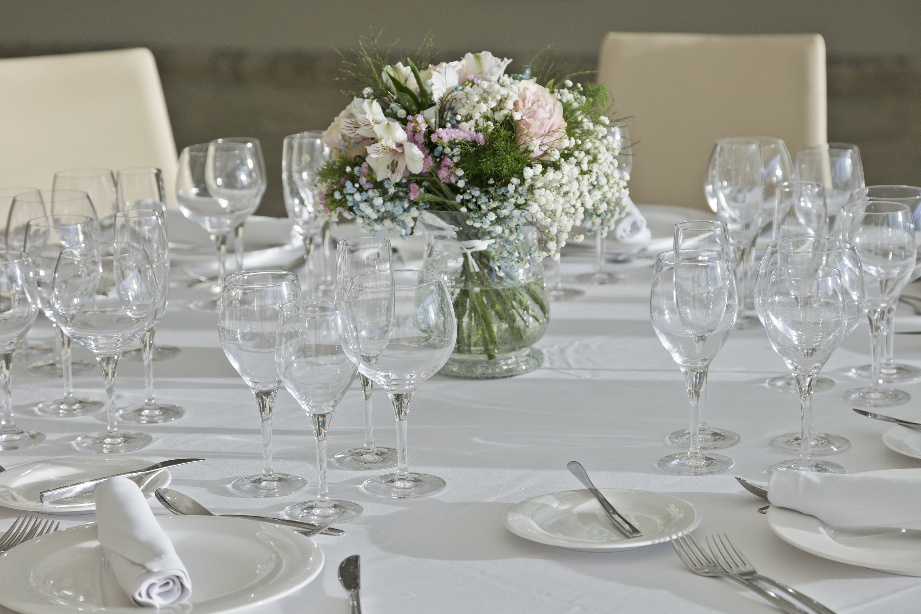 Elegant dining table set with white tablecloth, glasses, plates, and a floral centerpiece.