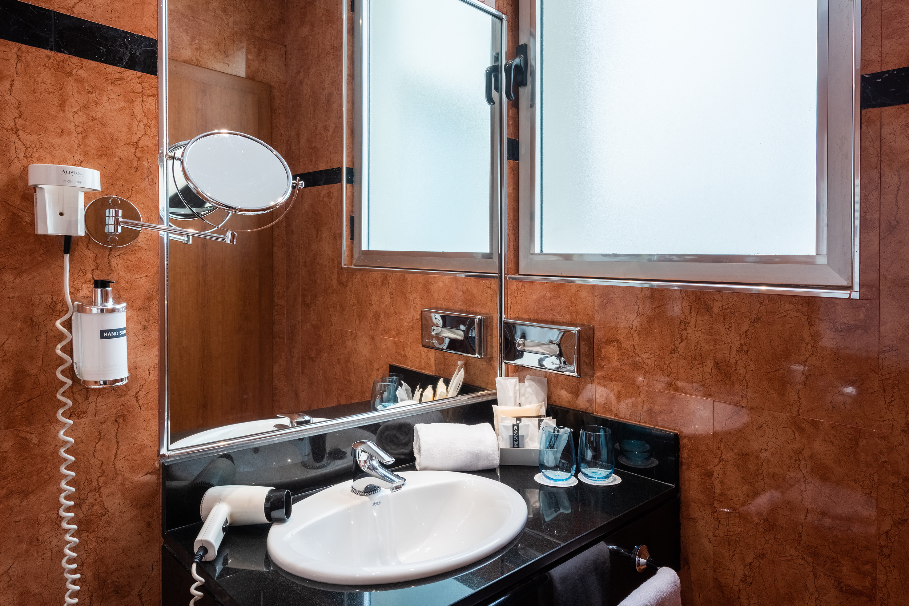 Hotel bathroom vanity with sink, mirror, hairdryer, and marble walls.