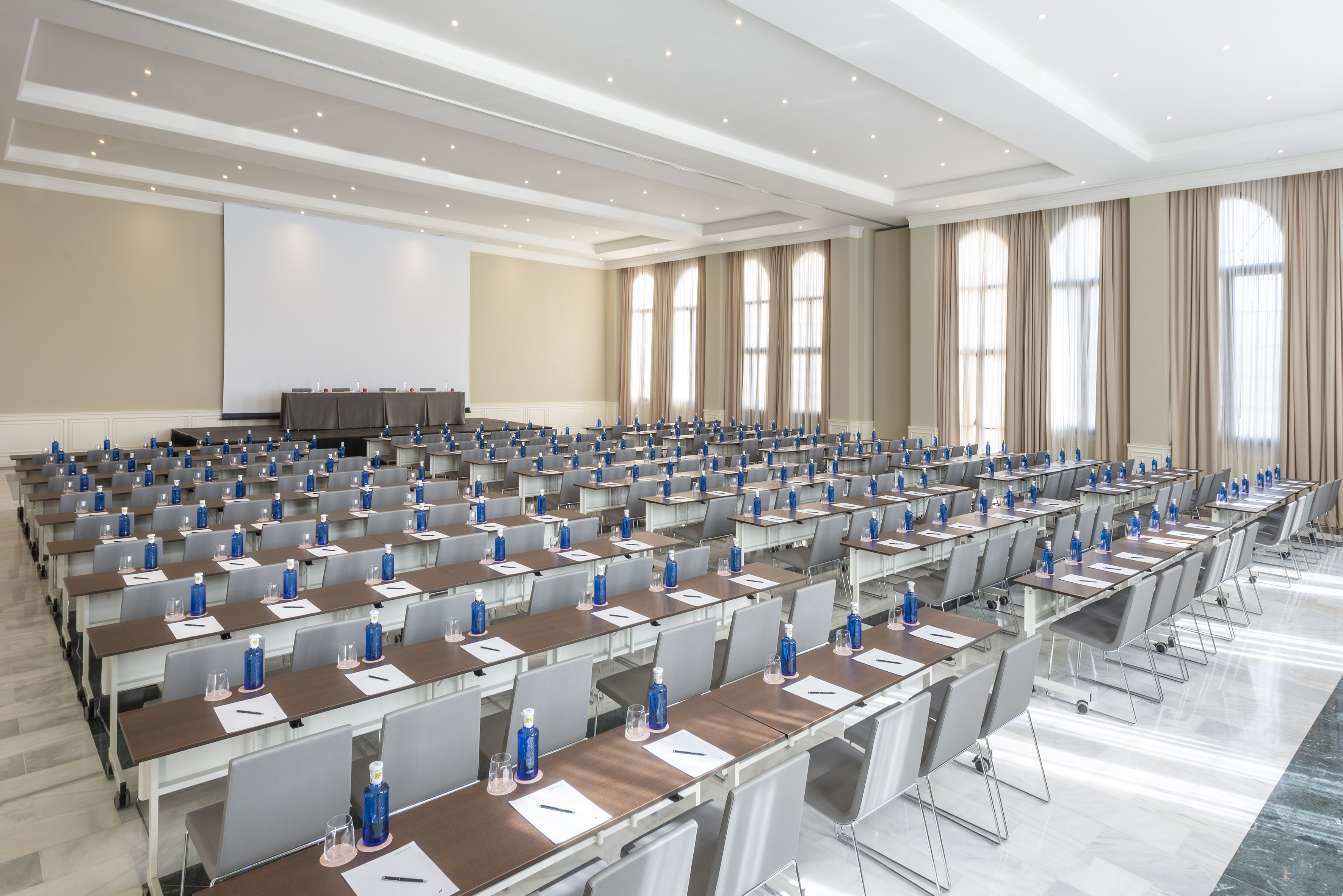 Spacious modern conference room with stage, screen, and rows of tables for meetings.