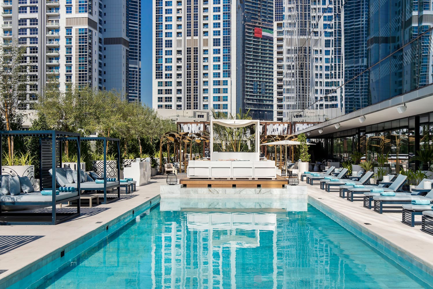 a pool with lounge chairs and trees in front of buildings