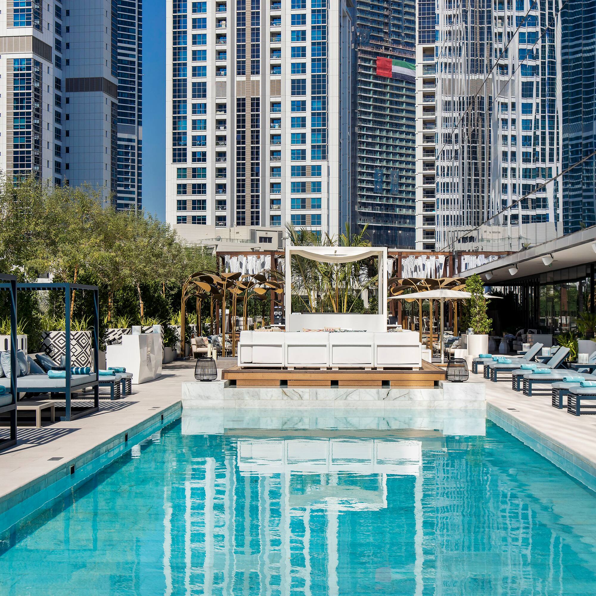 a pool with lounge chairs and trees in front of buildings
