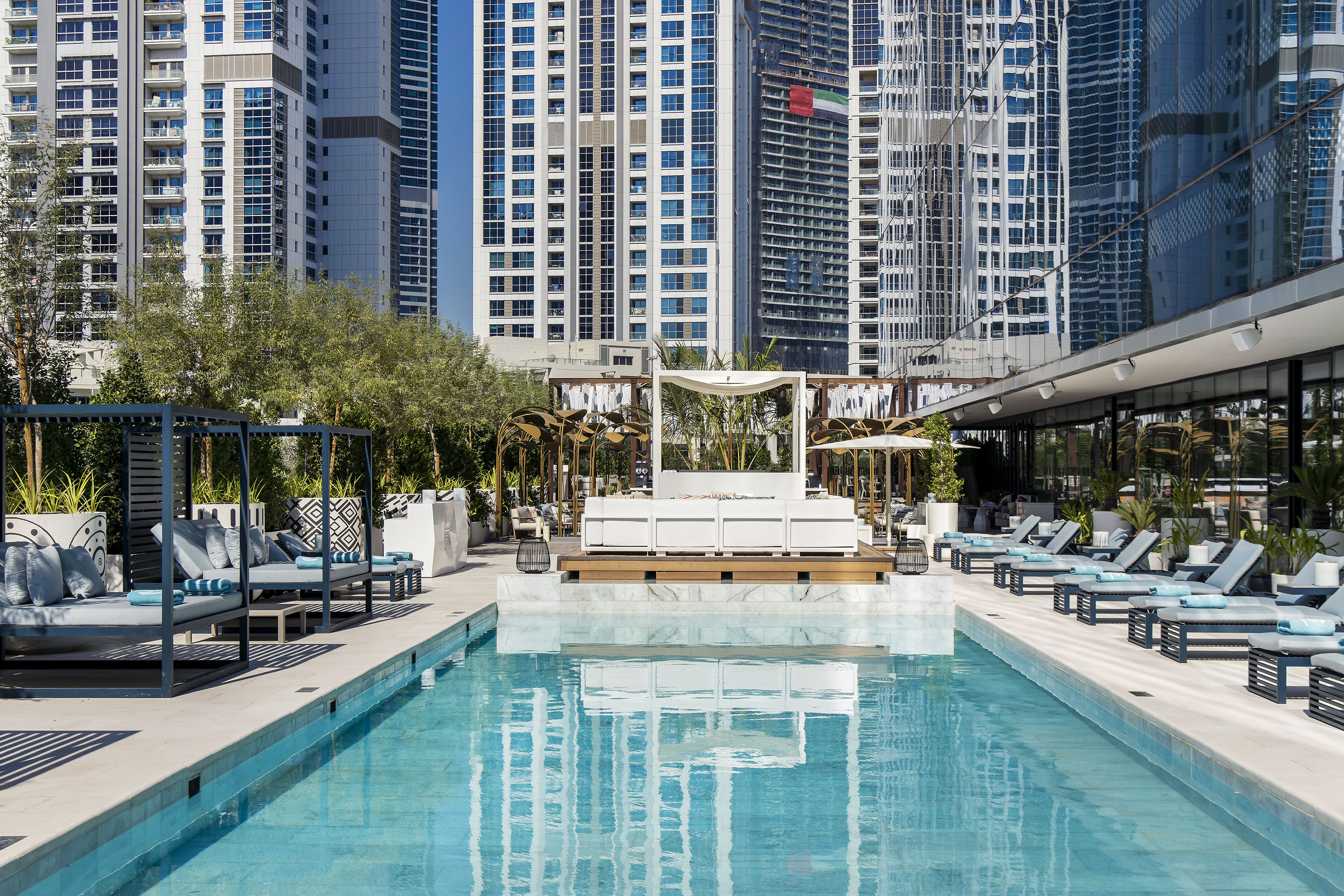 a pool with lounge chairs and trees in front of buildings