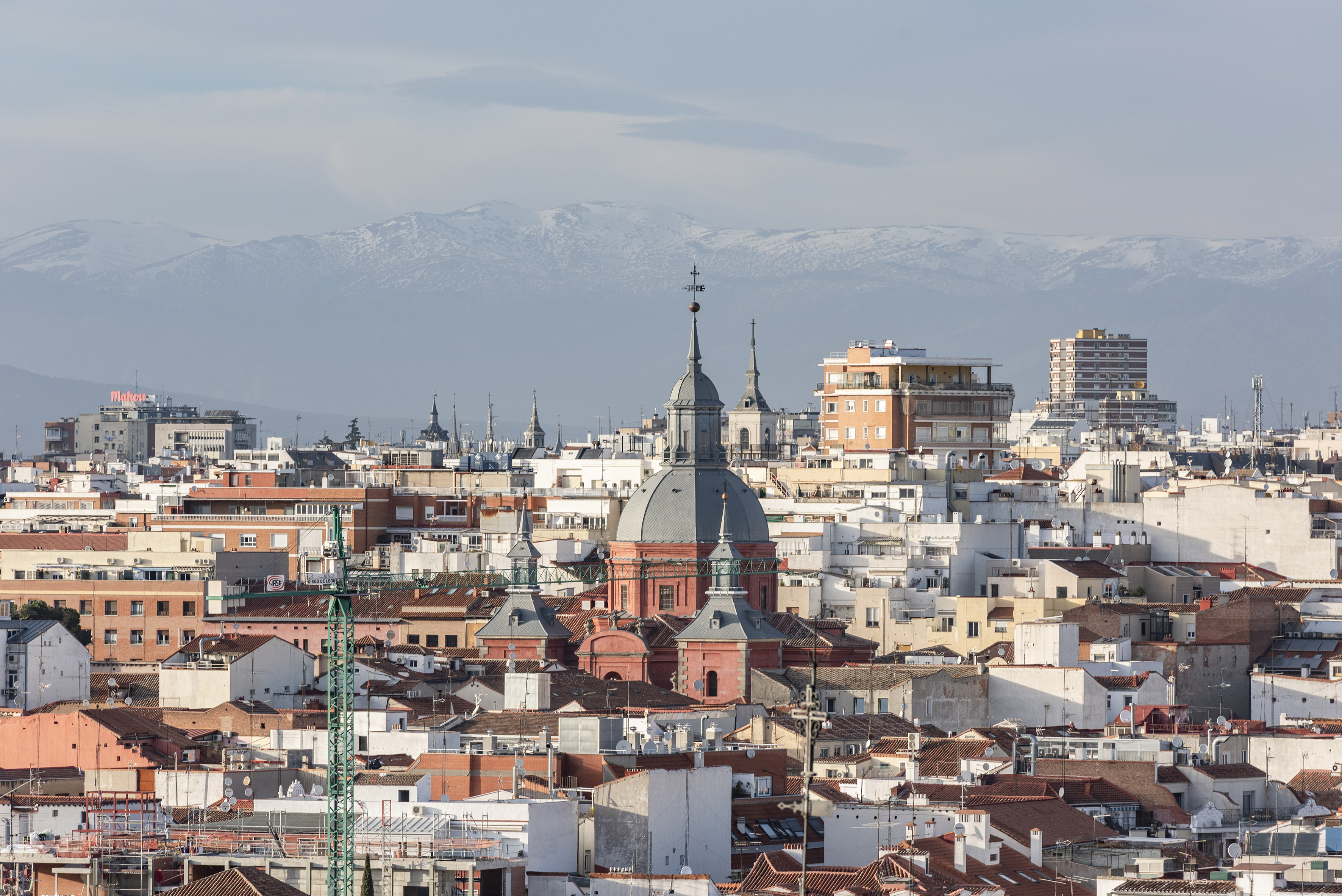 Madrid skyline with central dome, dense buildings, and snowy mountains.