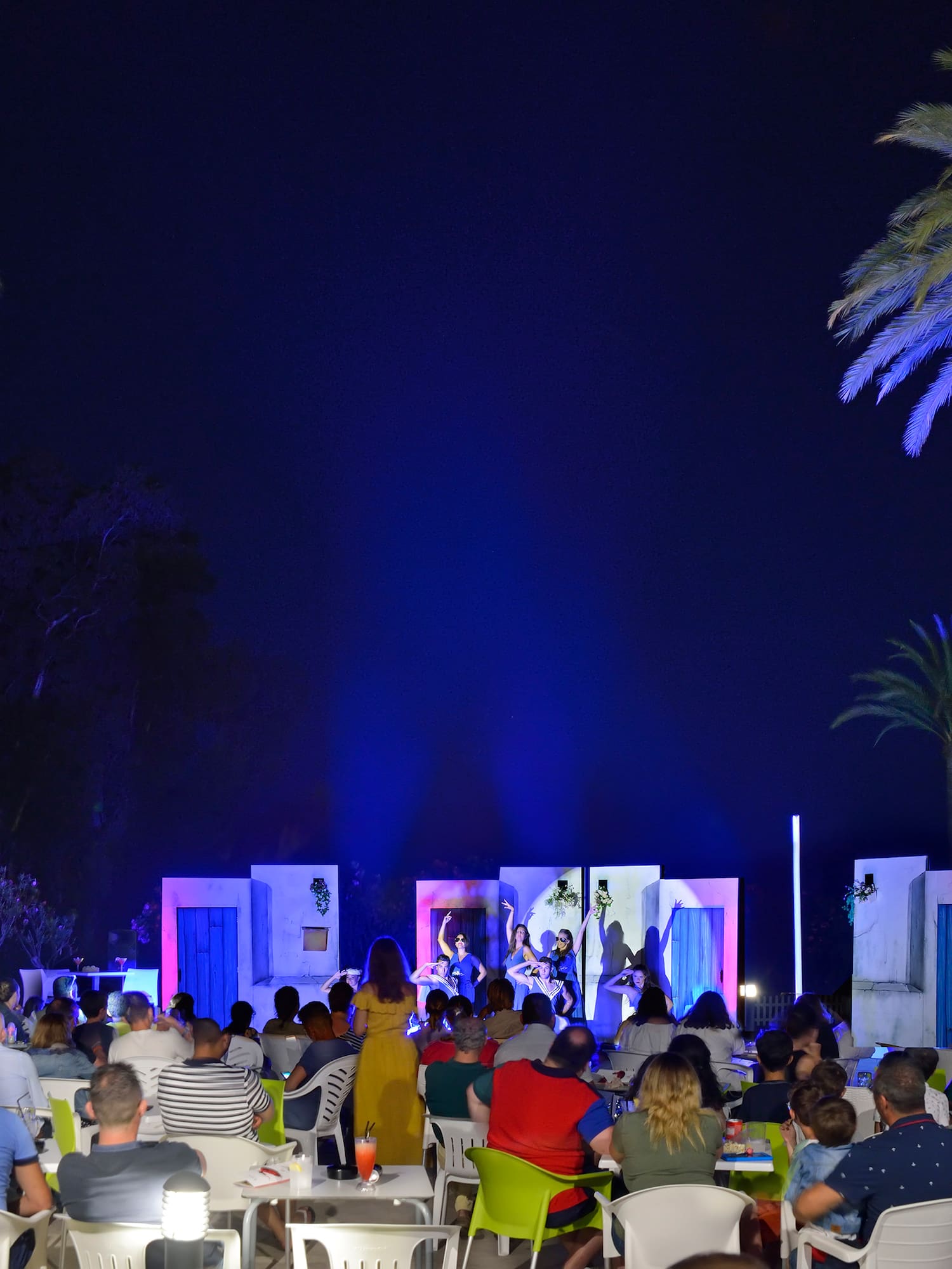 a group of people sitting in chairs and a stage with palm trees