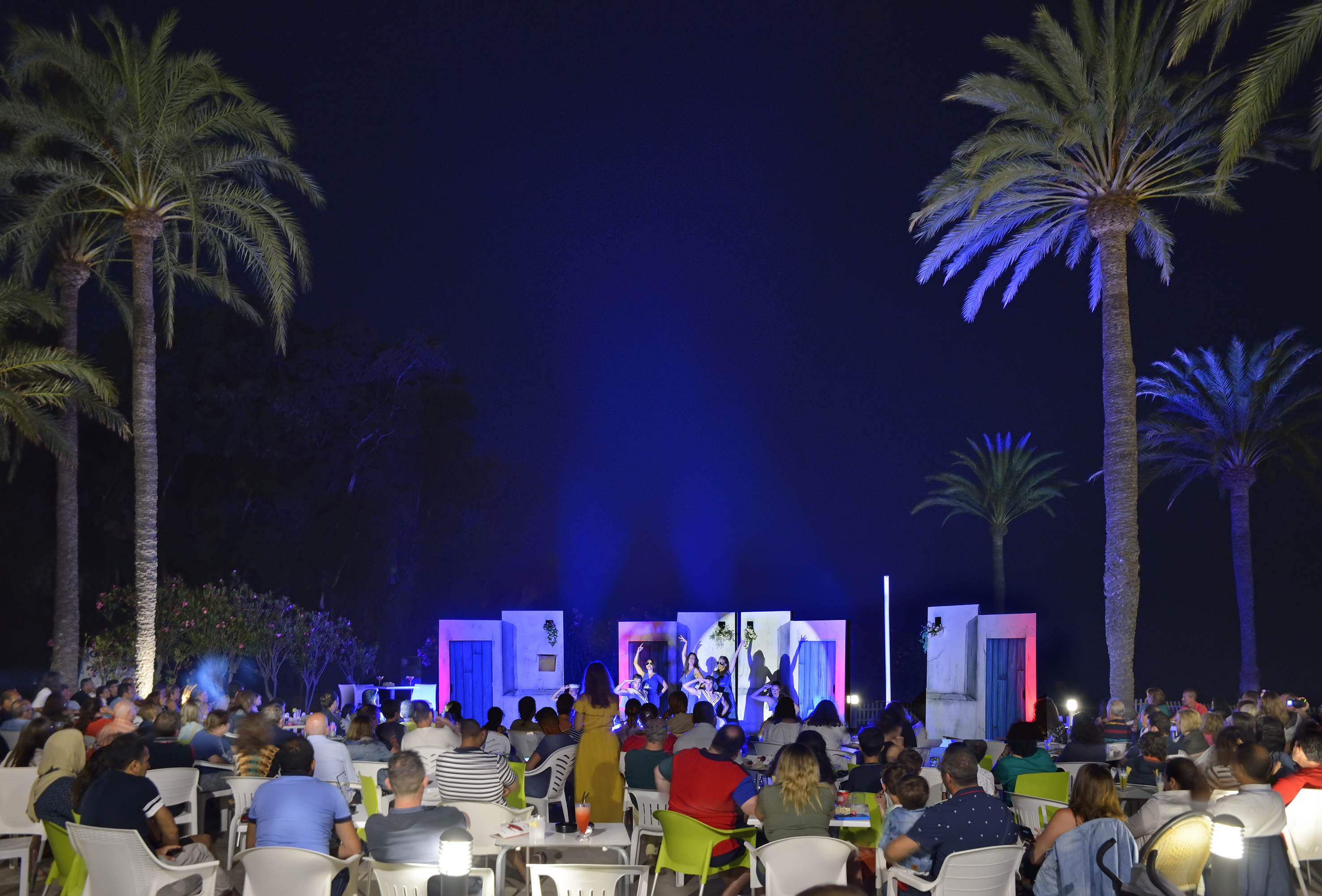 a group of people sitting in chairs and a stage with palm trees