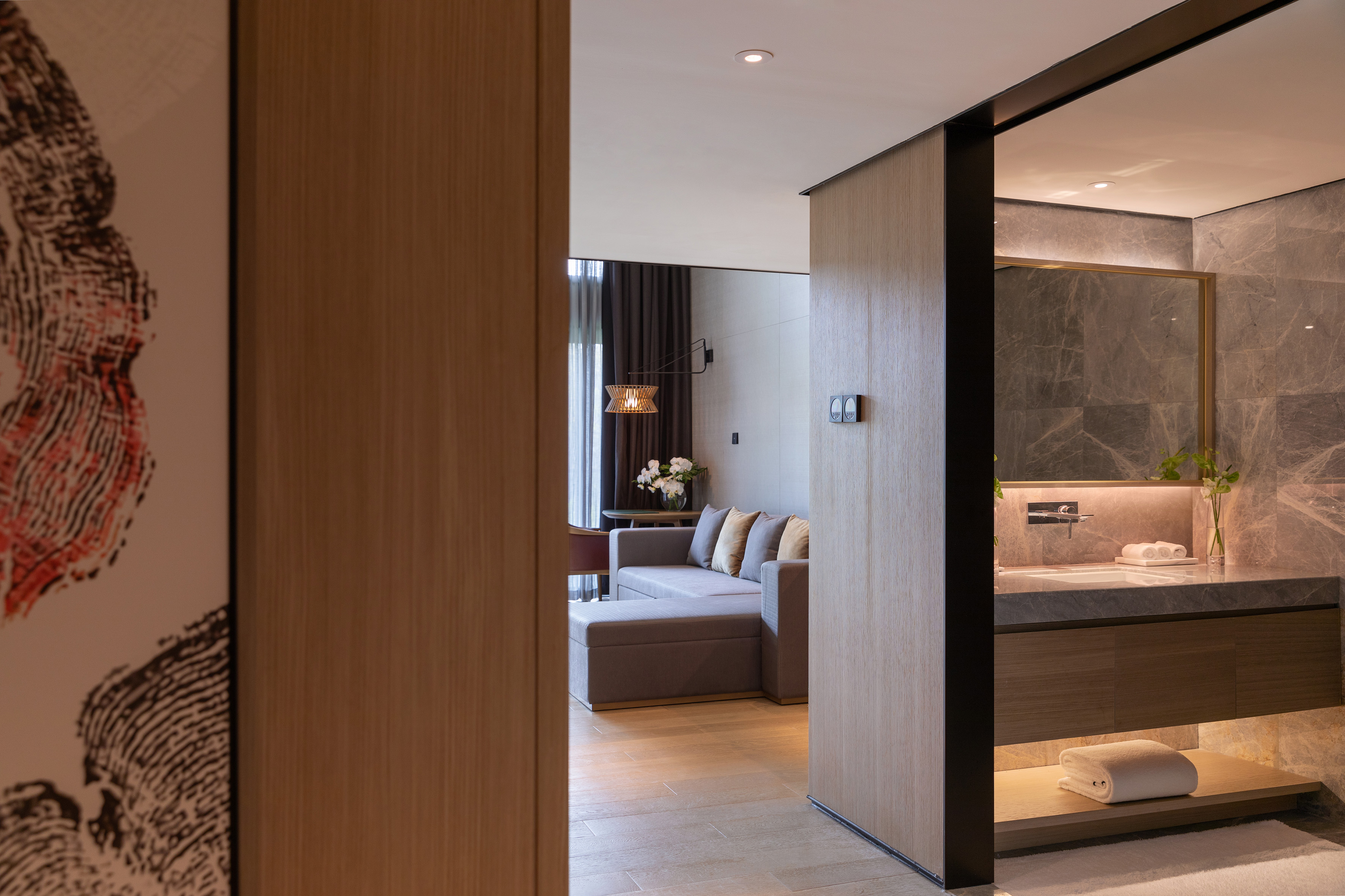 Open-plan luxury hotel suite with grey sofa and elegant marble bathroom.