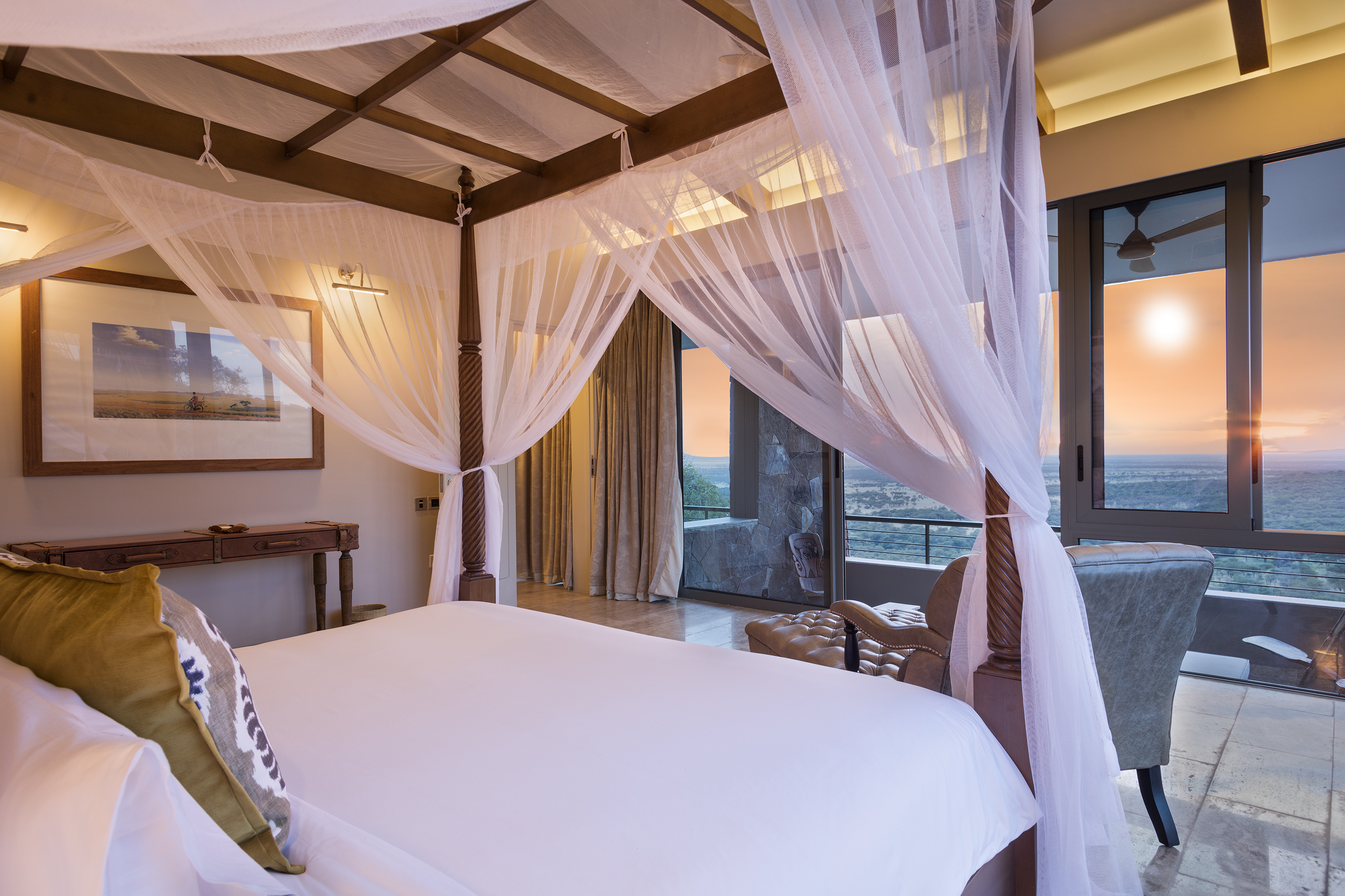 Luxury bedroom with four-poster bed, mosquito net, and savanna sunset view.