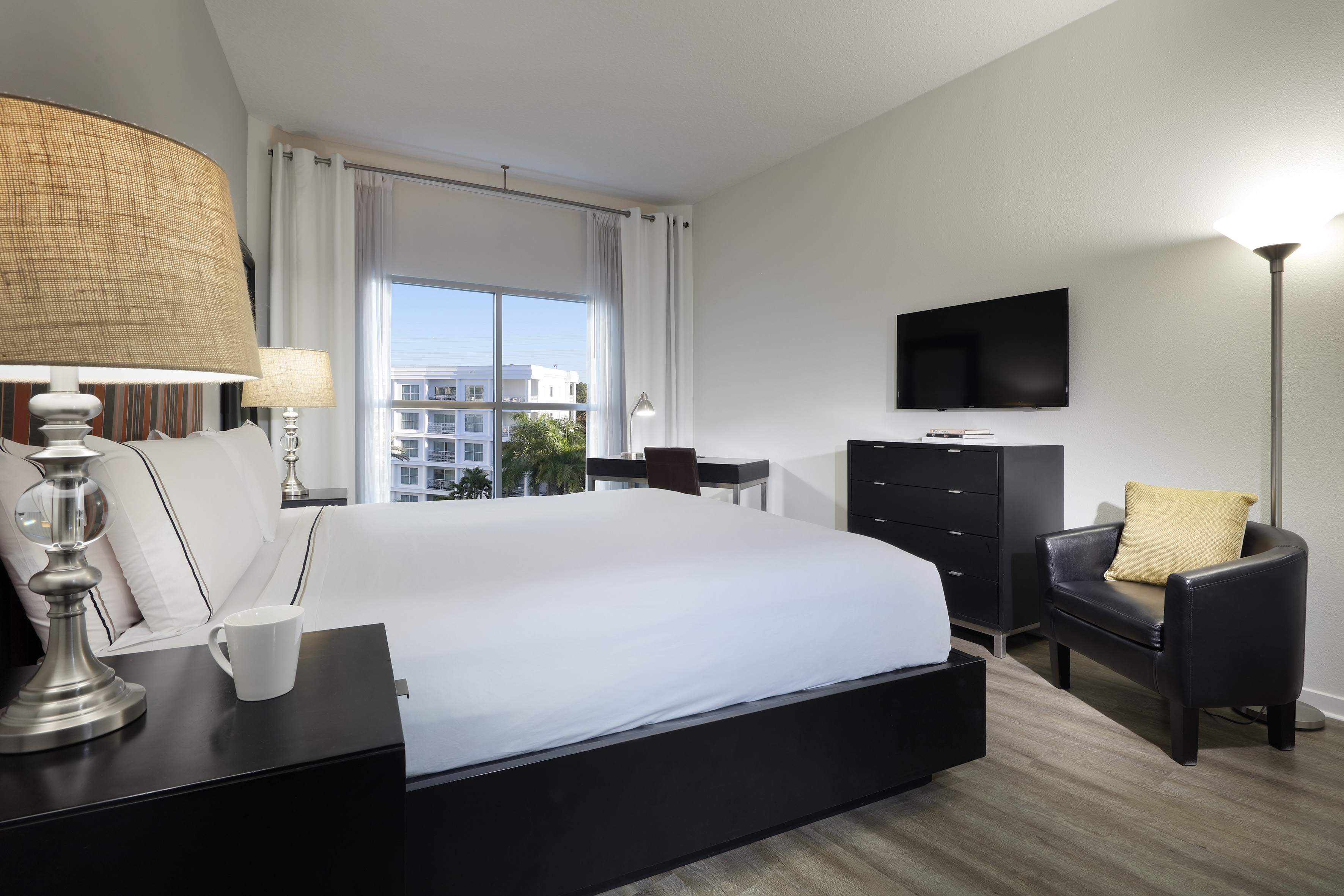 Modern bedroom with white bed, dark furniture, TV, desk, and bright window view. - Two-Bedroom Family Suite - Meliá Orlando Celebration, Orlando