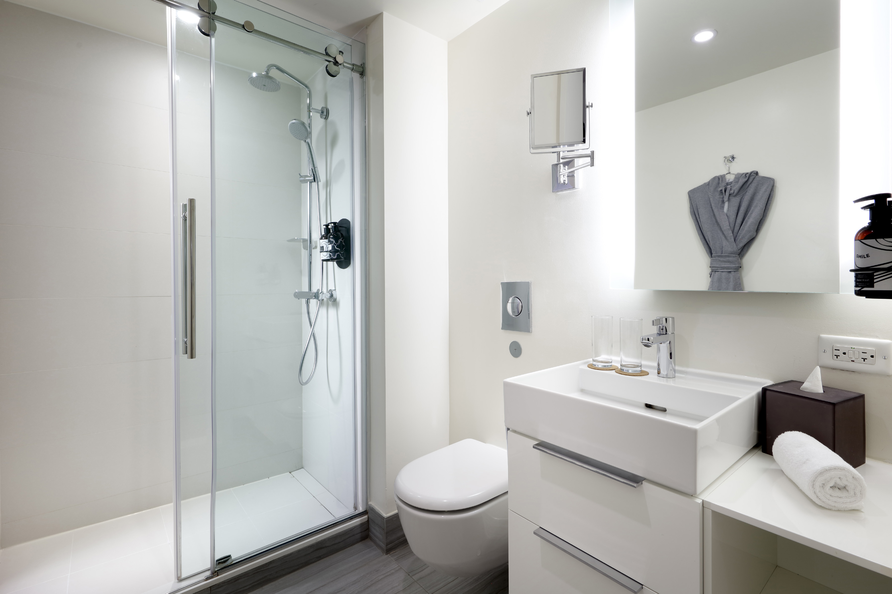 Bright modern bathroom with walk-in glass shower, white vanity, and toilet.
