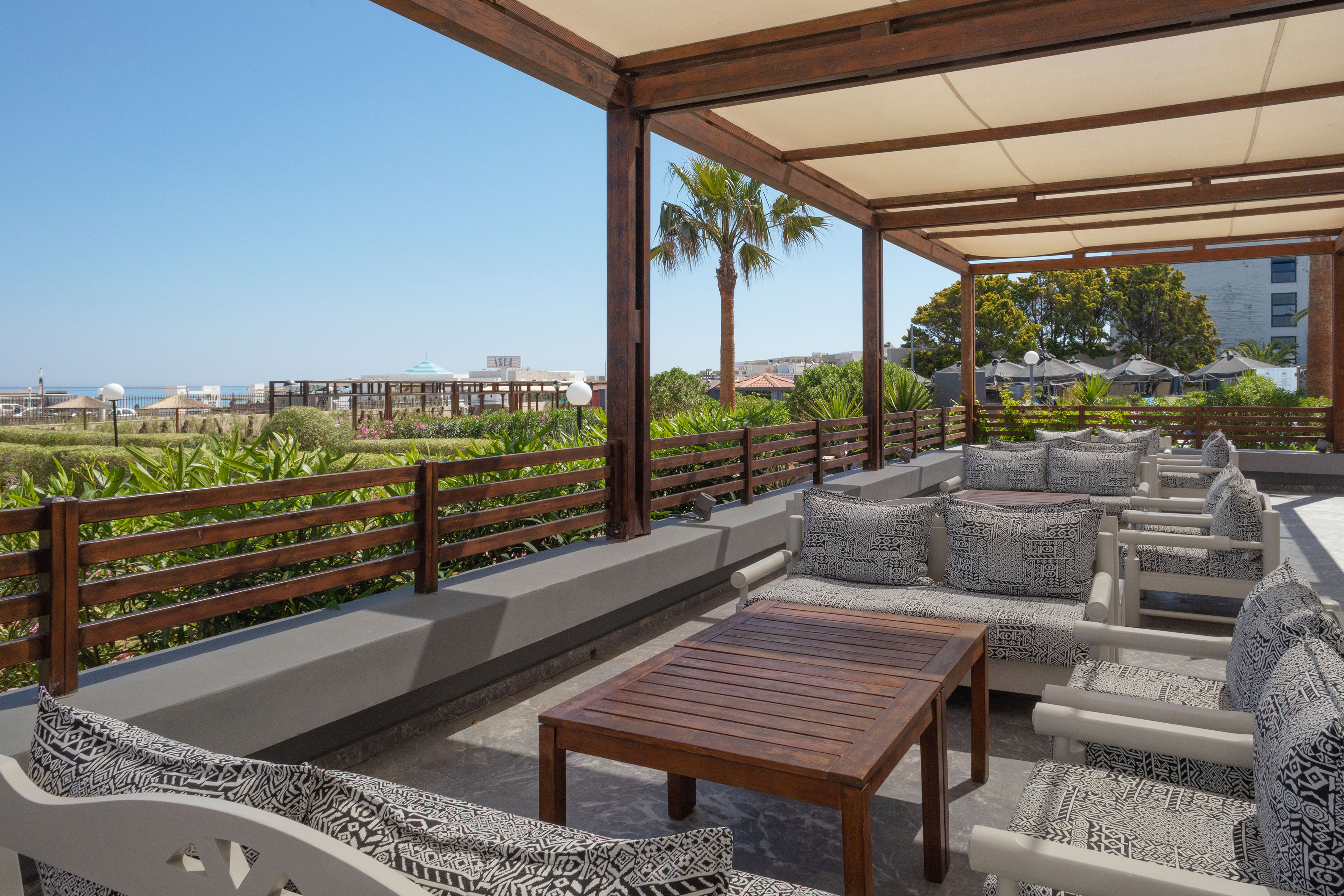 Shaded resort patio with ocean view, comfortable seating, and palm trees.