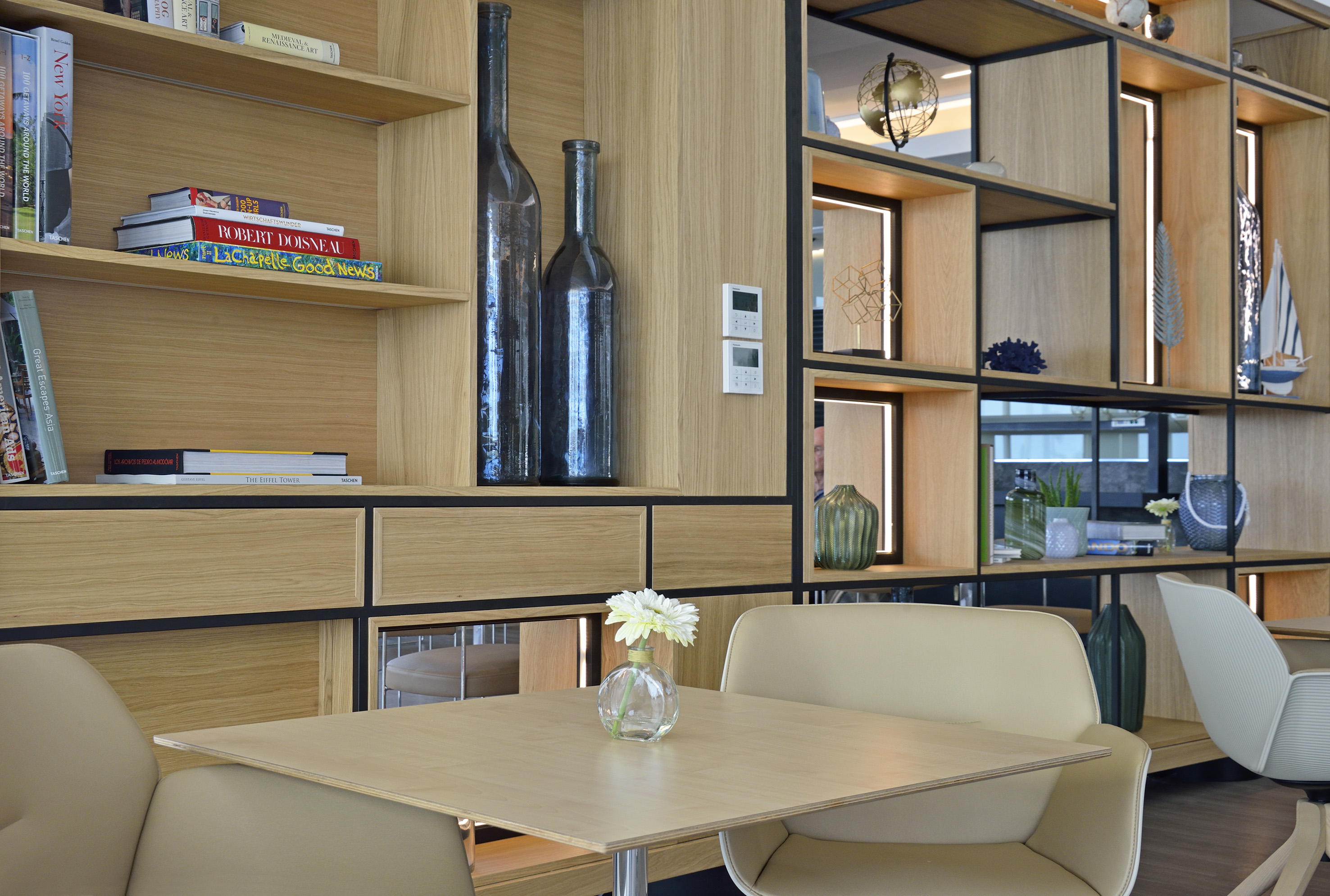 Modern lounge area with light wood table, chairs, and illuminated wooden bookshelves.